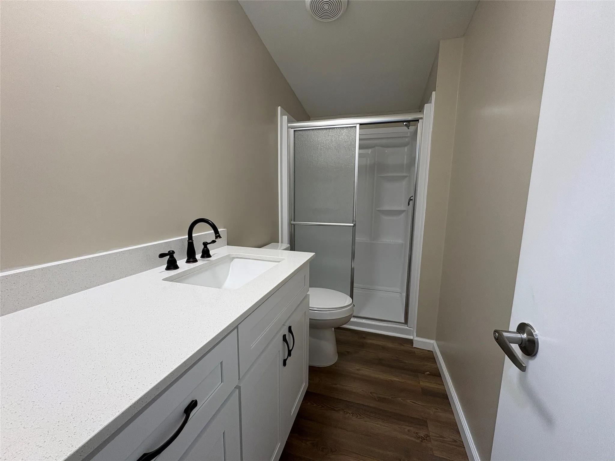 White vanity, granite counter top, integrated rectangular sink with matte black faucet, speckled light-toned countertop, and wood-finish flooring