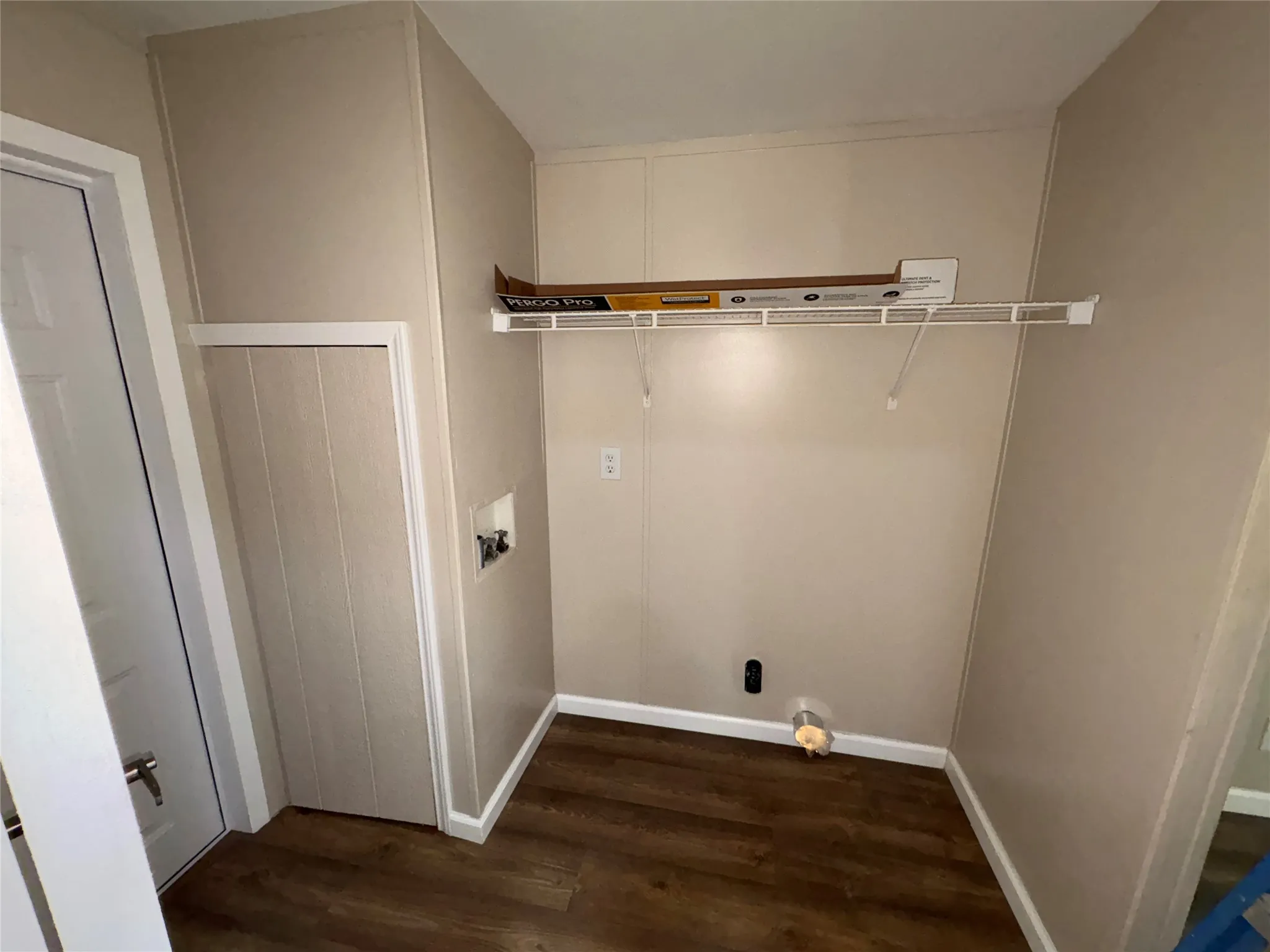 Wood-finish flooring with light-toned walls, featuring a bi-fold closet door, a white wire shelf, and washer hookups