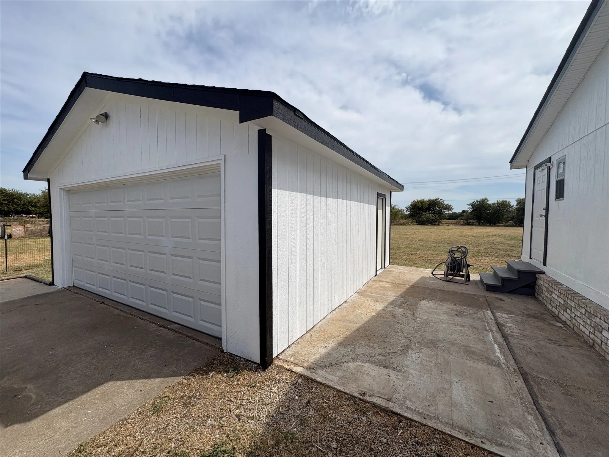 Detached garage with white panel siding, black trim, and a white paneled garage door