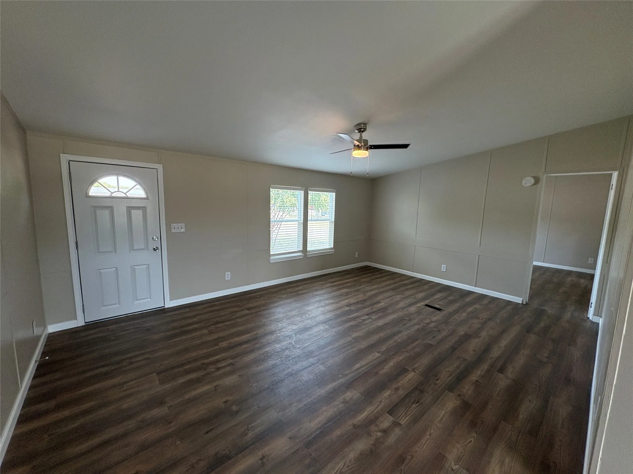 Spacious livingroom featuring wood-finish flooring, neutral-toned walls, multiple windows, and a ceiling fan with integrated lighting