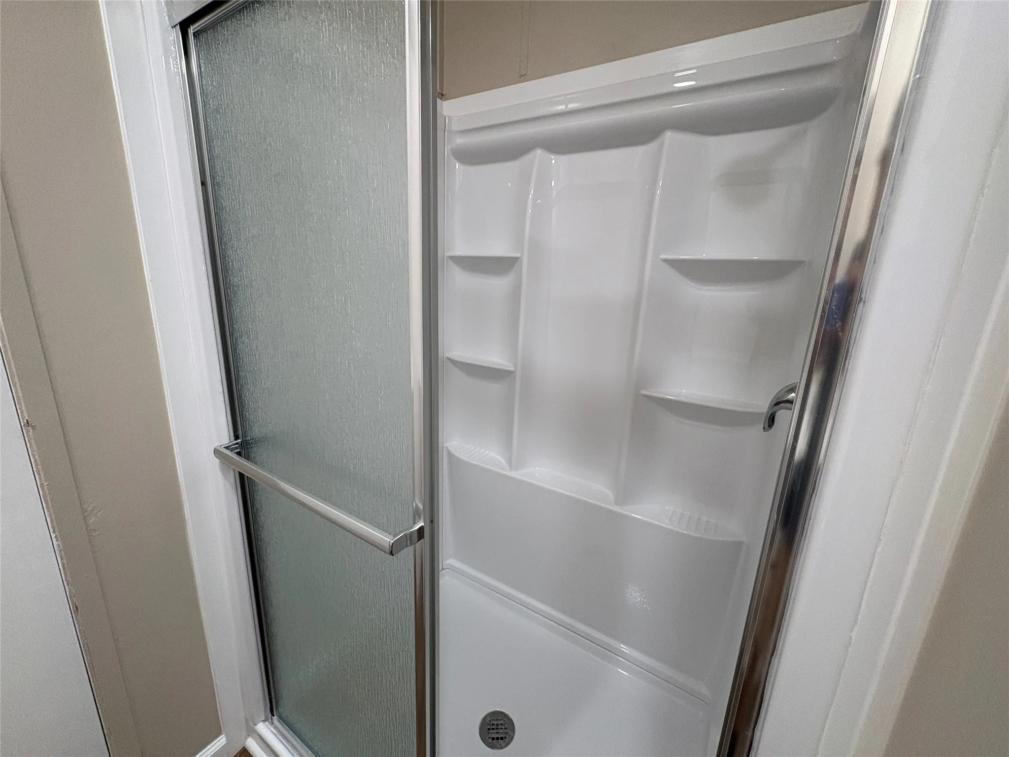 New shower enclosure with frosted glass door, chrome hardware, integrated shelving, and a built-in shower base