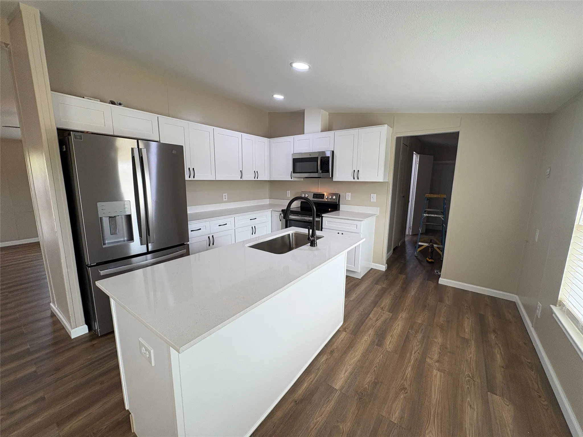 Kitchen featuring an island with an integrated sink, stainless steel appliances, white cabinetry, and wood-finish flooring