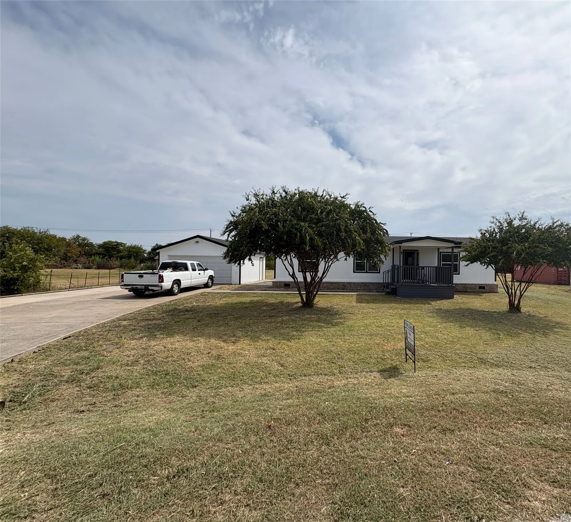 White exterior with dark trim accents, covered front porch, concrete driveway, attached garage, and mature landscaping