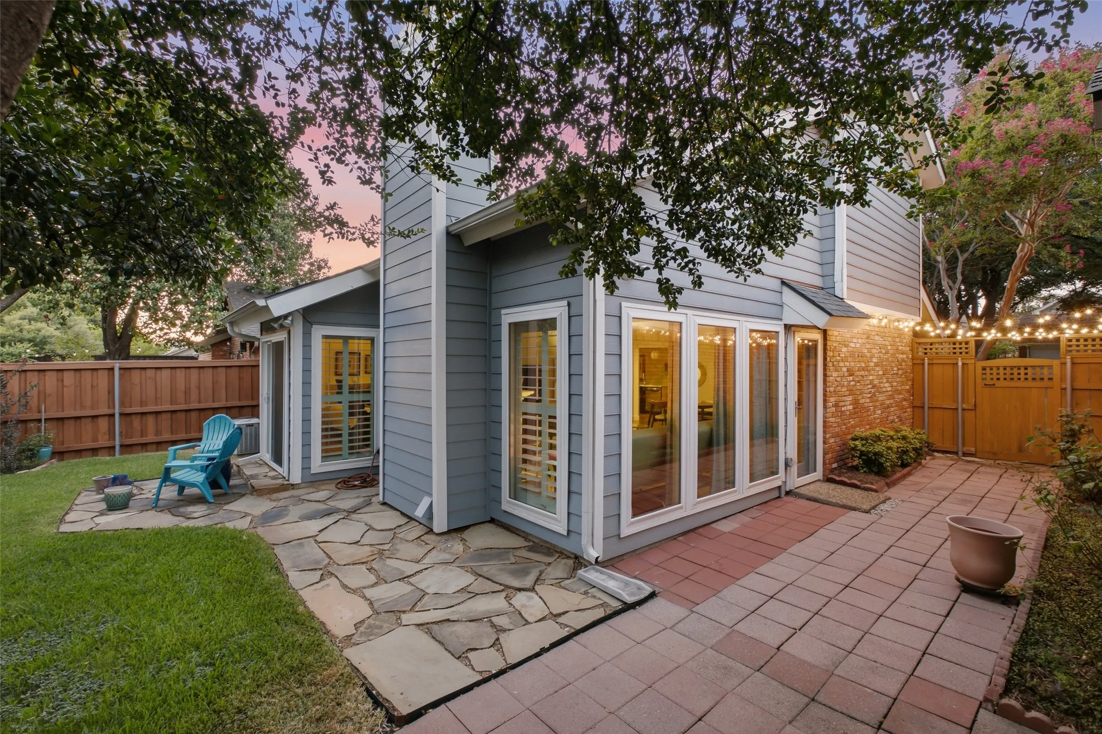 The rear exterior at dusk shows the home's generous glass — sliding doors and large windows that open the main living areas directly to the back patio, flagstone path, and yard.