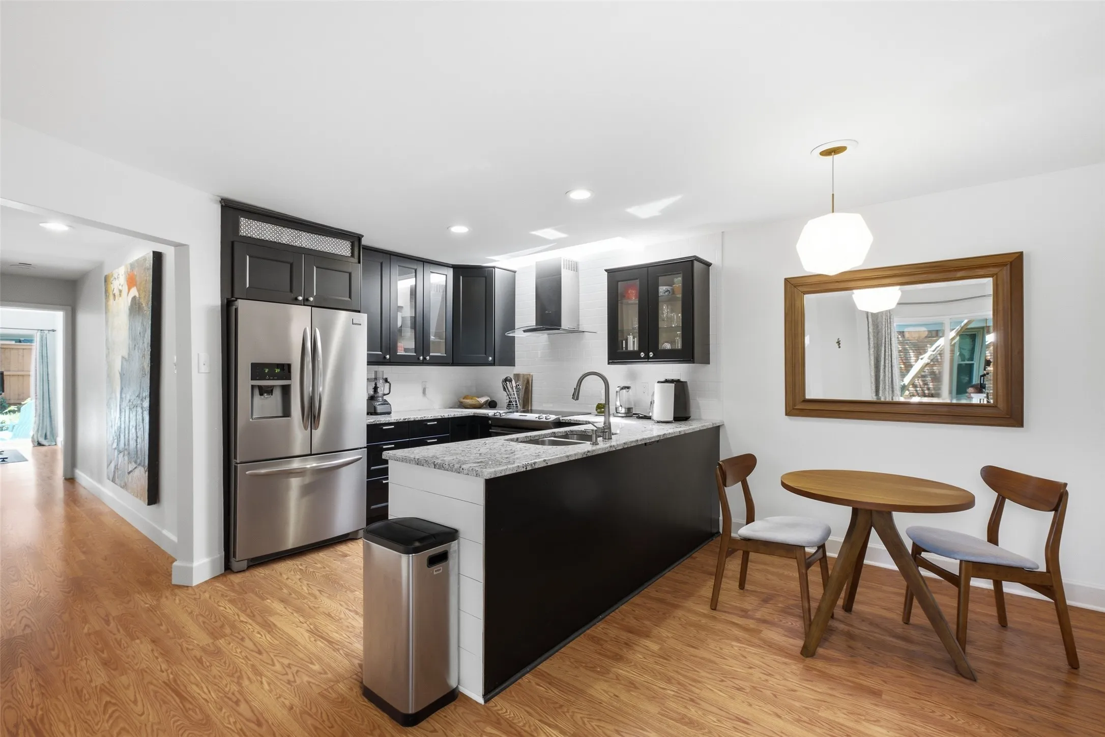 The kitchen features black shaker cabinets, granite countertops, stainless steel appliances, a range hood, and a peninsula with bar seating — plus a breakfast nook with its own pendant light.