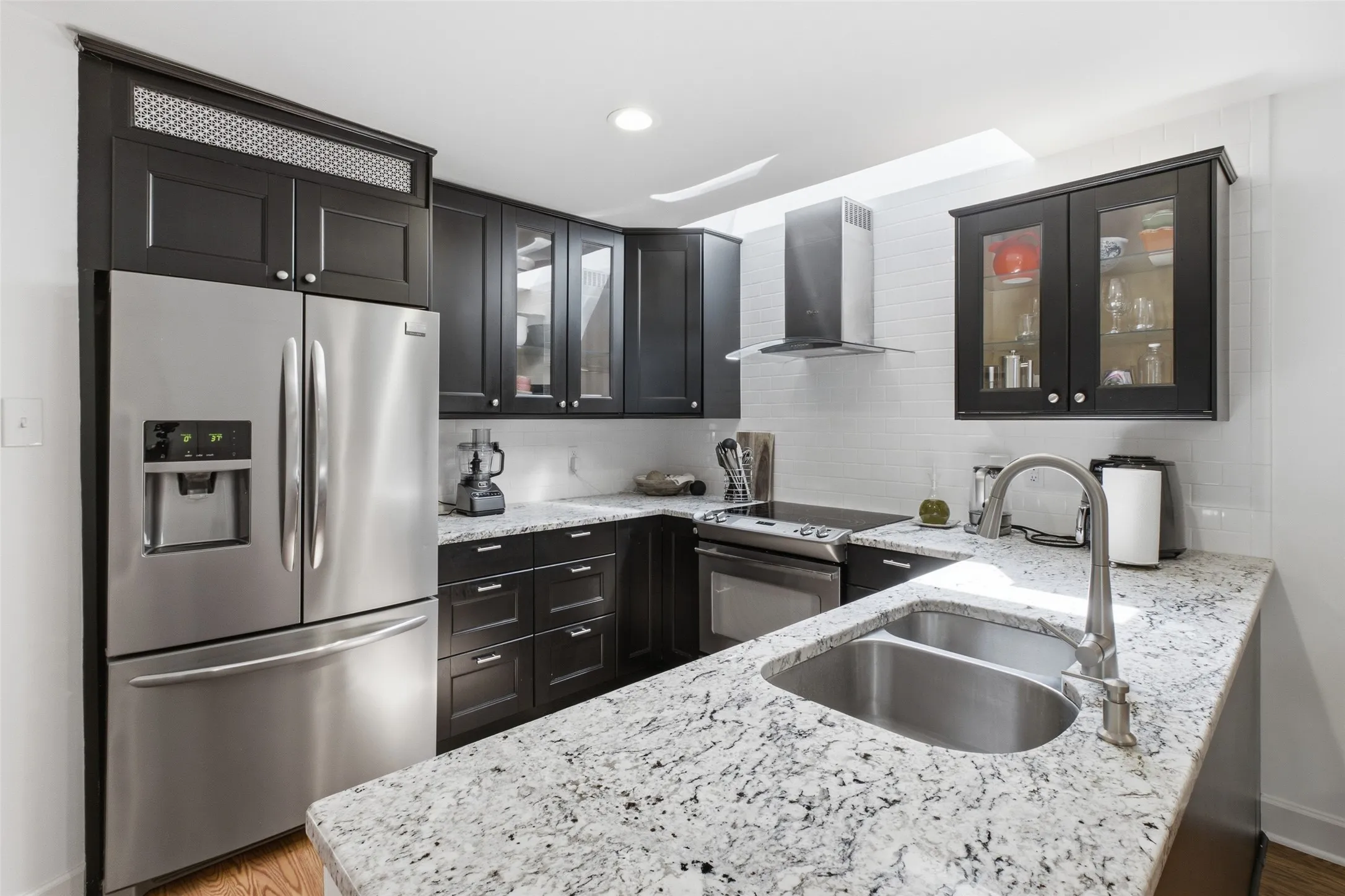 A closer look at the kitchen details: granite counters with deep veining, a double stainless sink, glass-front upper cabinets, and a full stainless appliance suite including range and dishwasher.
