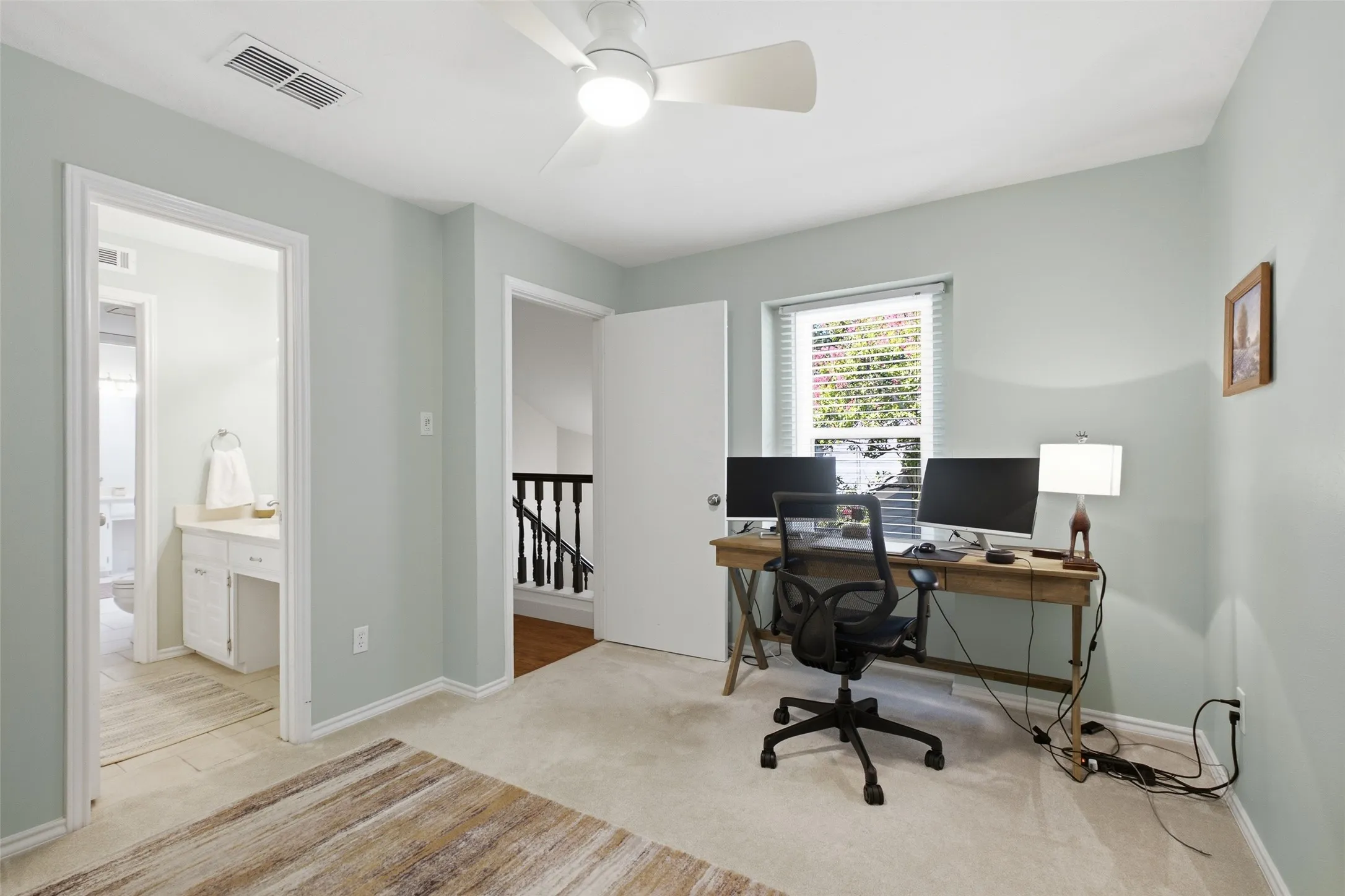 The third upstairs room functions well as a home office or bedroom — with a window overlooking the front yard, a ceiling fan, carpet, and an attached bath just steps away.
