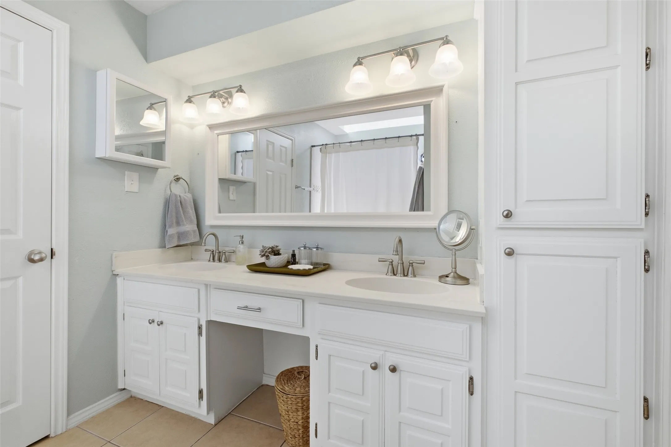 The primary bath features double vanities, white cabinetry with brushed nickel hardware, a wide mirror, and an abundance of cabinet and counter space on both sides.