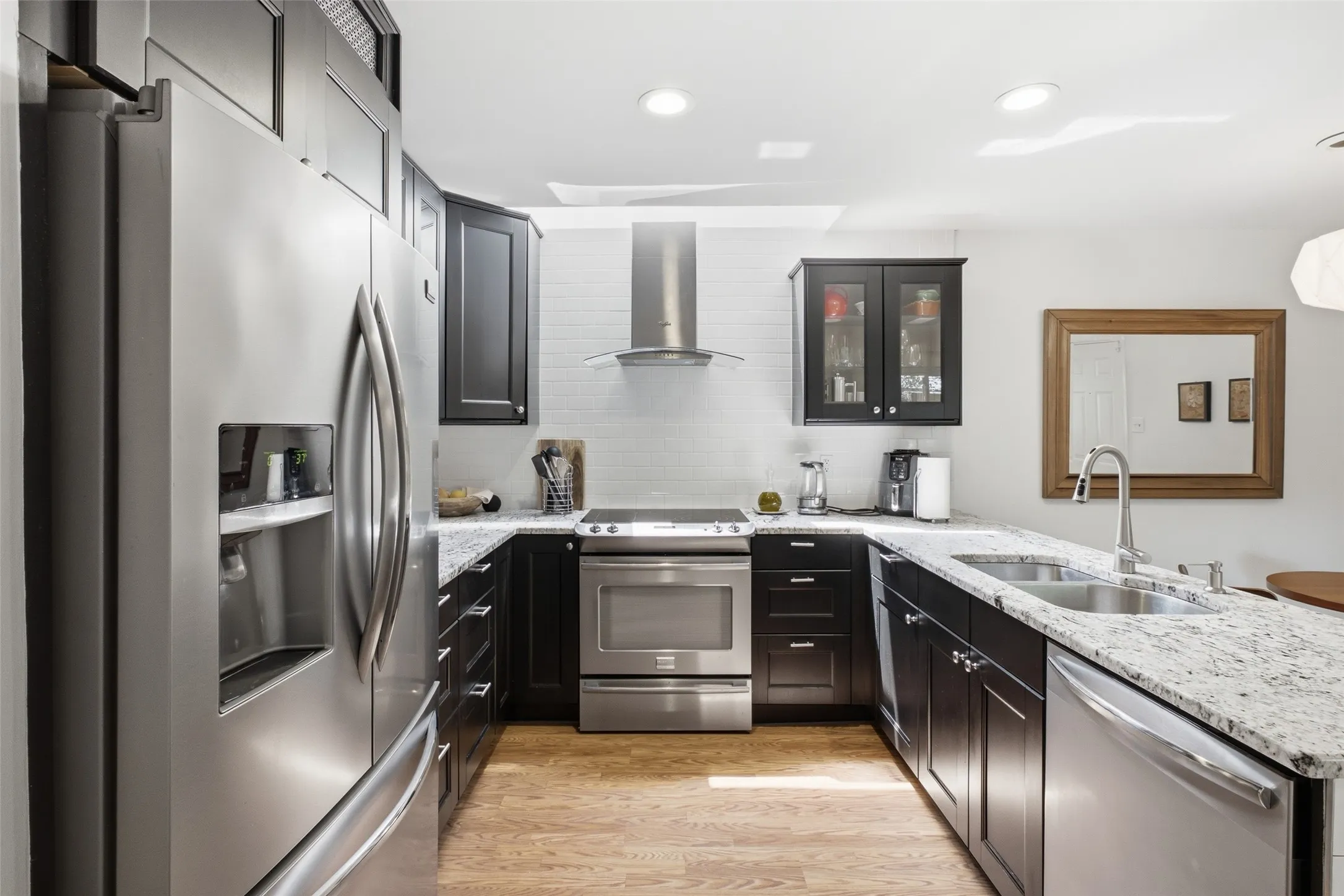The full kitchen layout — wraparound granite counters, a French-door refrigerator, a chef-style range with hood, and a skylight that keeps the workspace naturally bright throughout the day.