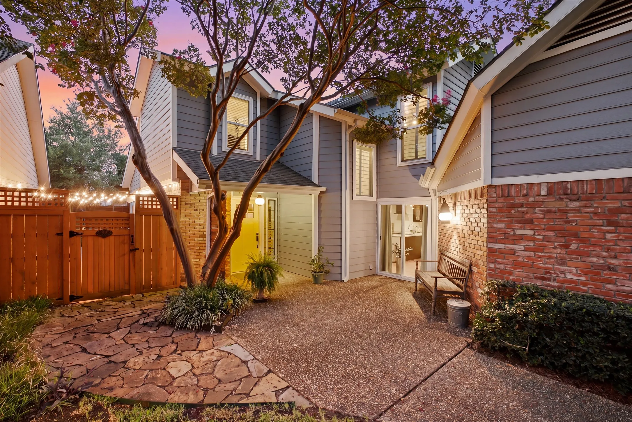 An entry with flagstone pathways, mature crape myrtle, and warm wall sconces sets a welcoming tone before you even step inside.