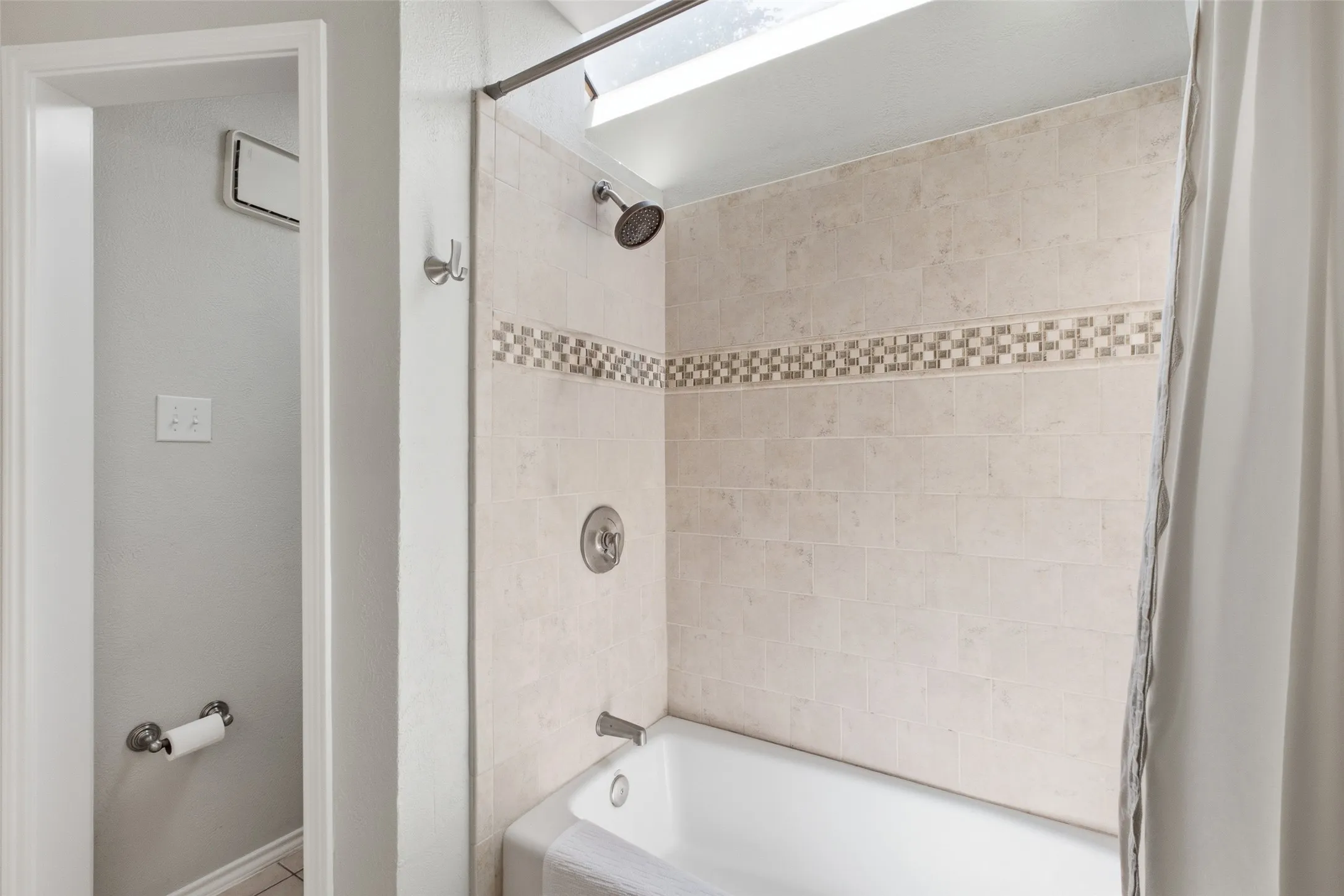 A skylight over the tub-and-shower combo fills this primary bath with natural light. The tile surround features a classic mosaic accent border — a small but well-considered detail.