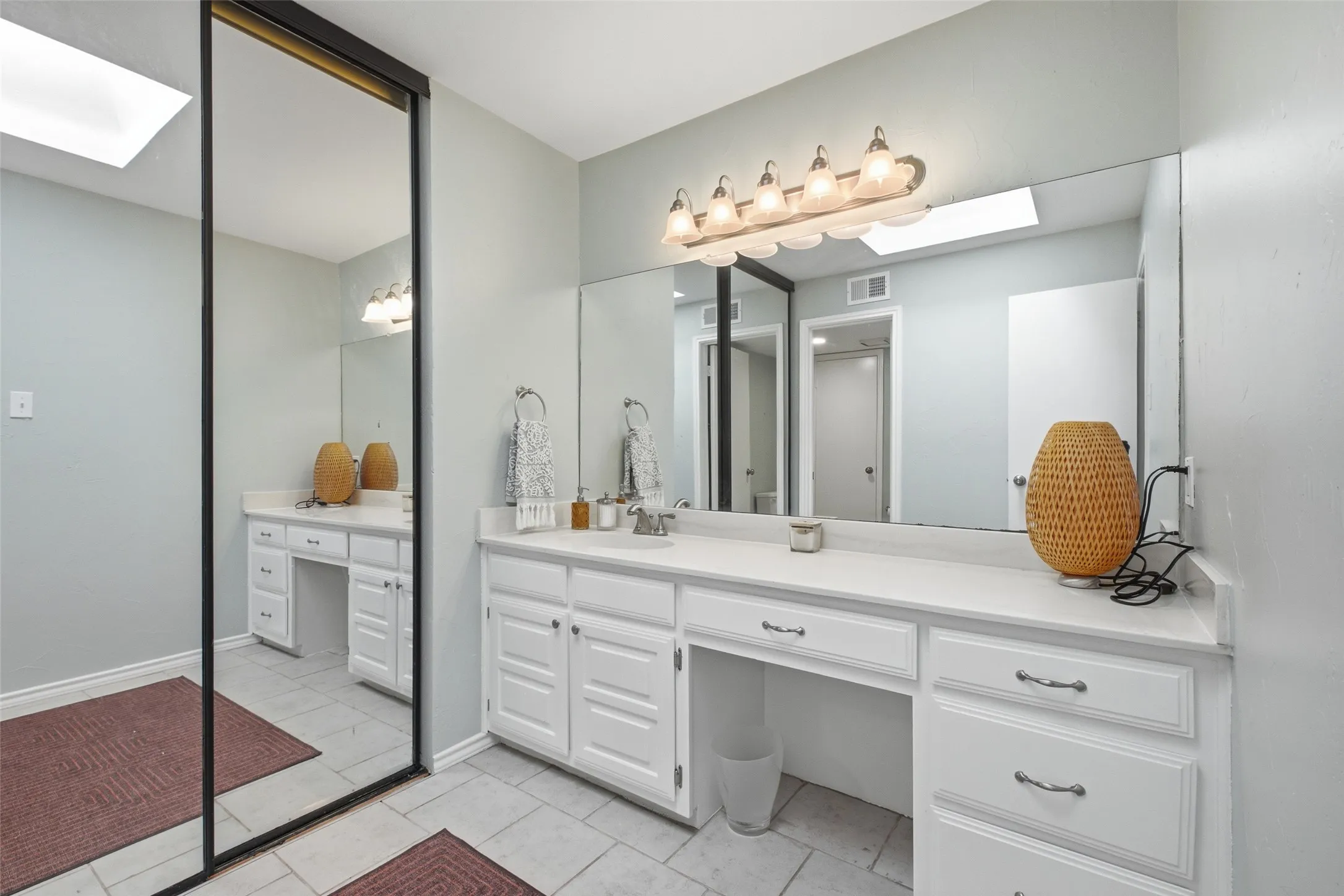The upstairs bath shared by the second bedroom features a skylit vanity, full-width mirror, white cabinetry, and a separate toilet and tub room for added privacy.