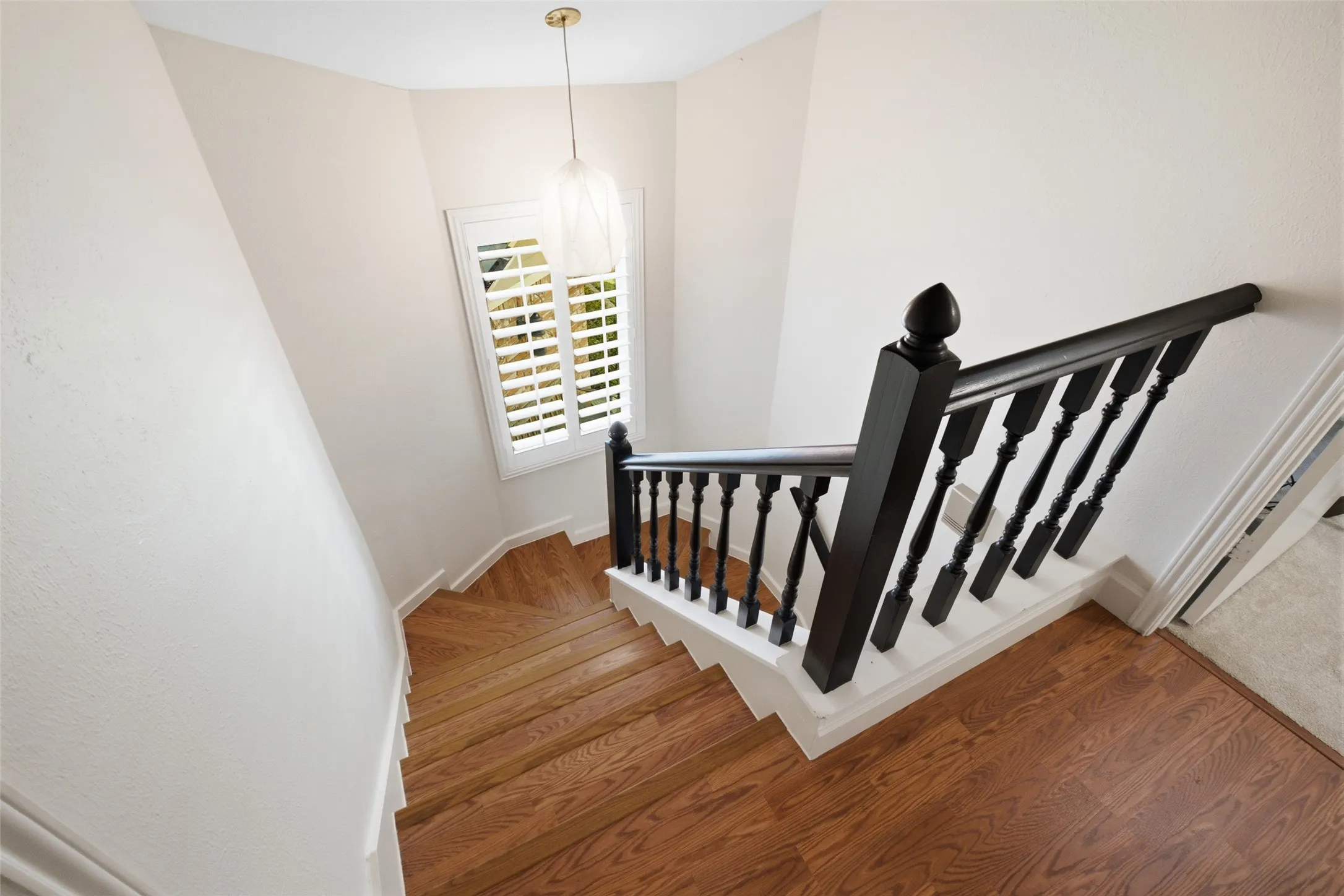 The staircase is a nice architectural moment — black painted balusters, white risers, hardwood treads, and a delicate pendant overhead lighting the landing.