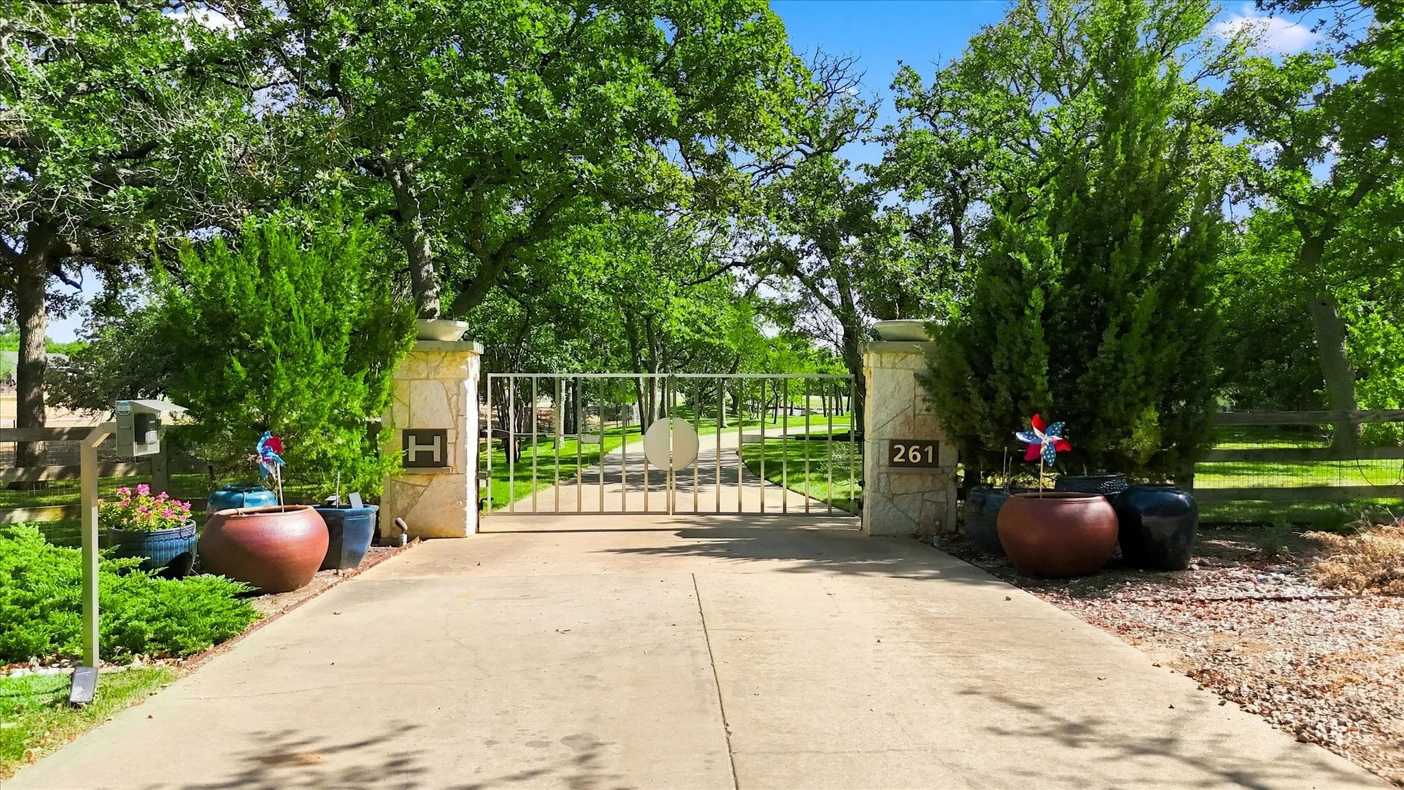 Gated entrance featuring decorative wrought-iron gates and substantial stone pillars, leading to a tree-lined driveway