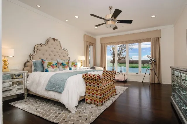 Hardwood flooring, tufted upholstered headboard, recessed lighting, ceiling fan, and expansive window with water scenery