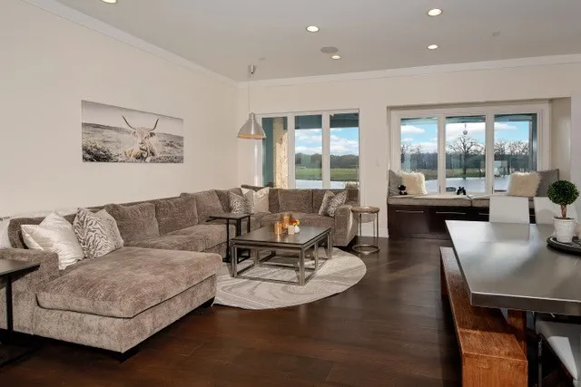Expansive dark wood-finish flooring, recessed lighting, white crown molding, and large windows with a built-in window seat