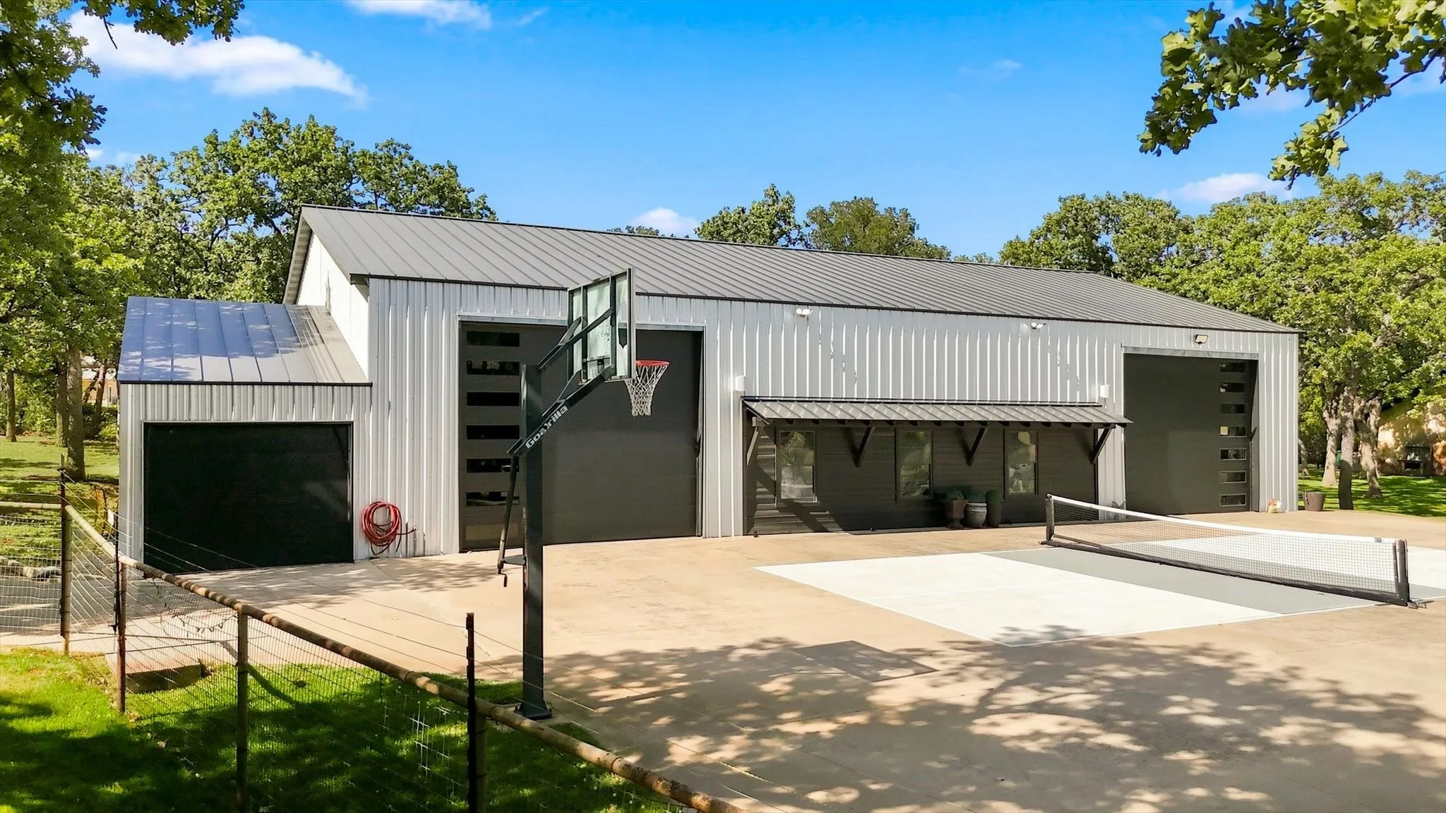 Metal-sided structure with multiple garage doors, concrete sports court, and an awning-covered outdoor area