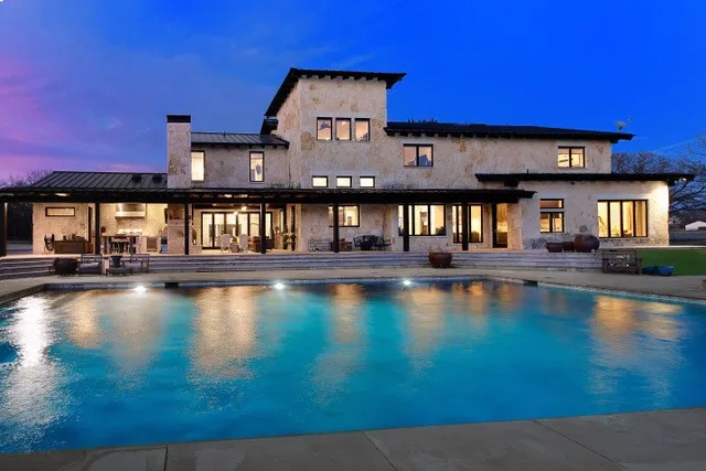 Stone exterior residence with an expansive swimming pool and a covered patio featuring an outdoor kitchen