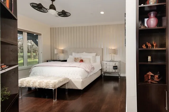 Hardwood flooring throughout, large window, ceiling fan with light, built-in shelving, and striped wall treatment