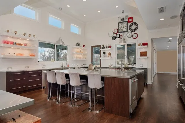Expansive kitchen with vaulted ceilings, wood-finish flooring, a large island with seating, a stainless steel countertop, and built-in shelving