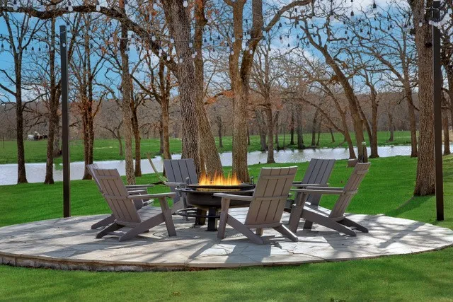 Stone patio with a built-in fire pit, surrounded by mature trees and manicured lawn