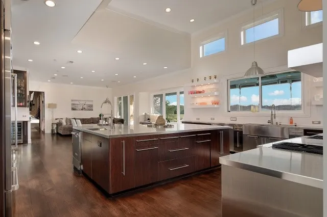 Spacious kitchen with a large central island, stainless steel appliances, wood-finish flooring, and high ceilings with transom windows