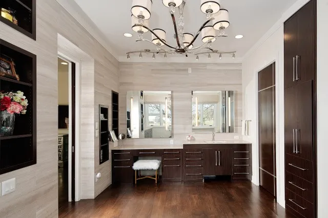 Hardwood flooring, custom built-in cabinetry, dual vanity with undermount sinks, wall-mounted mirrors, and an elegant chandelier