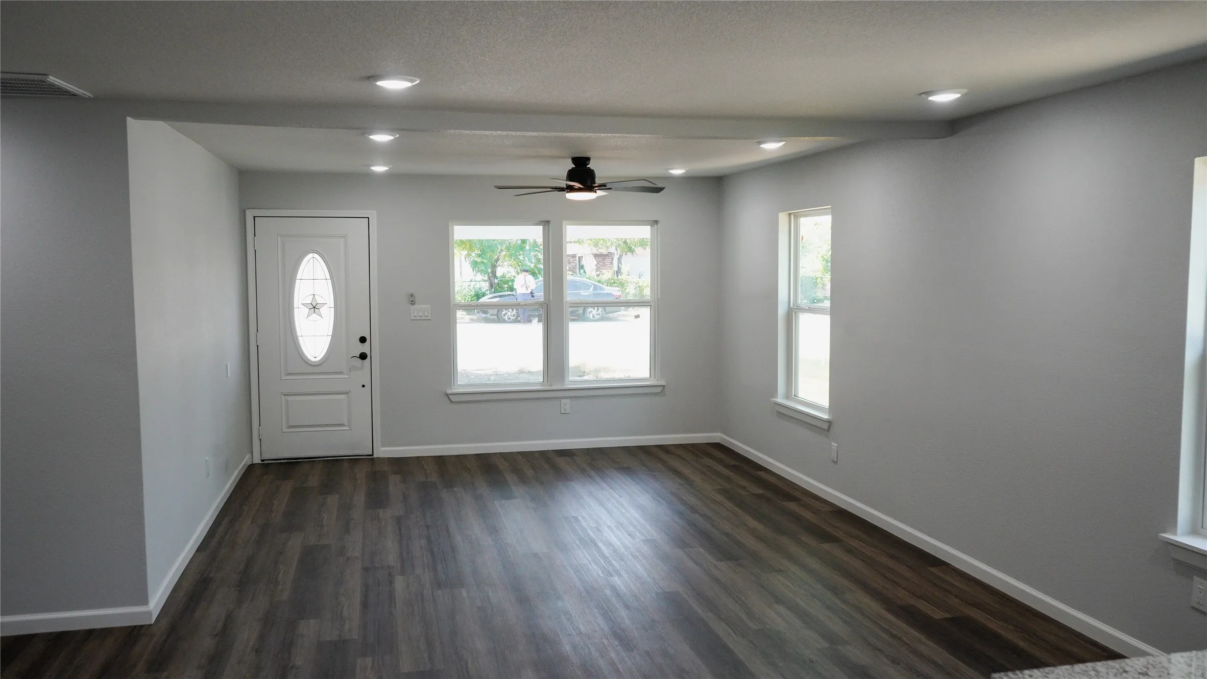 Wood-finish flooring, recessed lighting, ceiling fan, multiple windows, and a white entry door with an oval-shaped glass insert