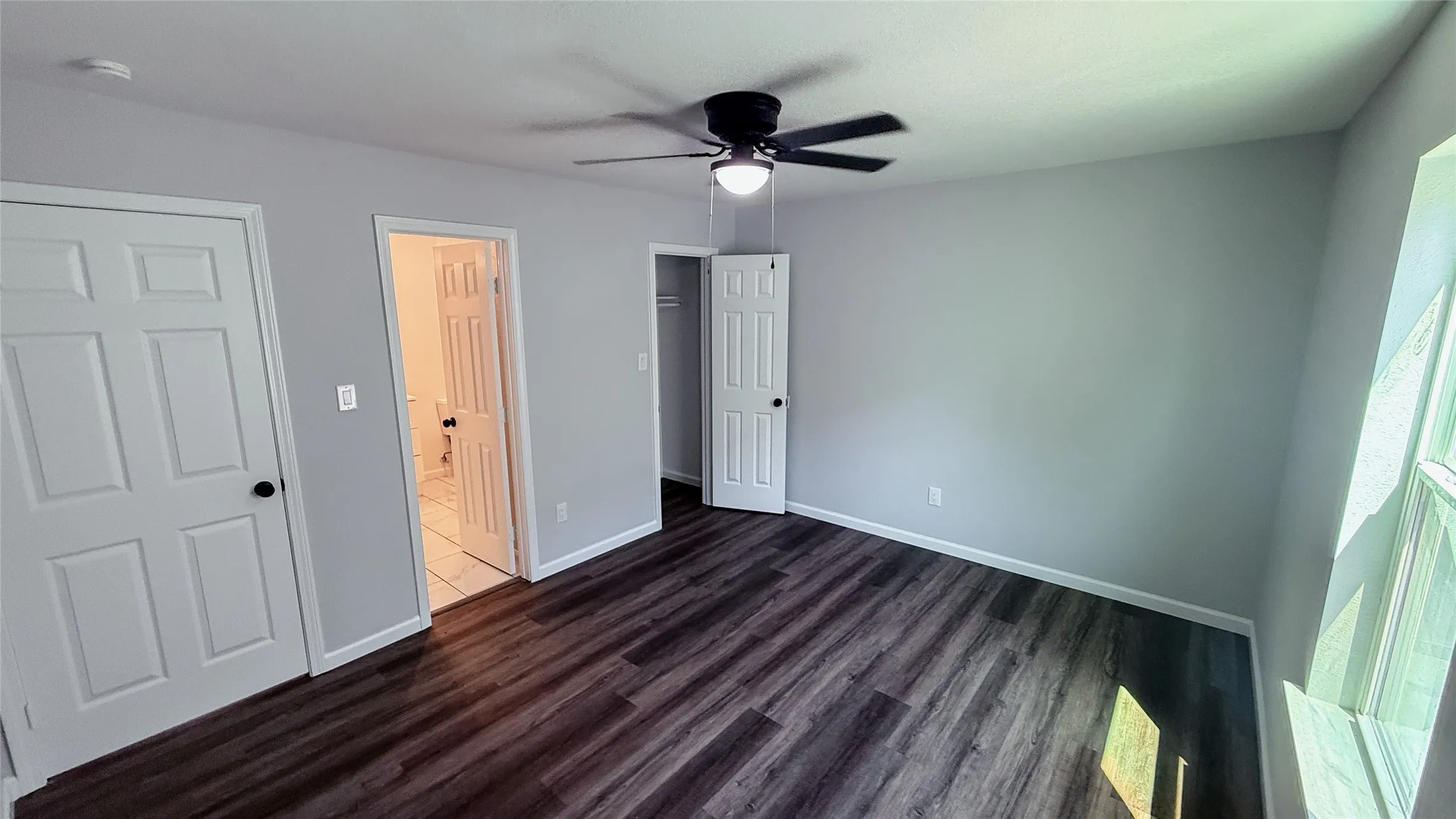 Wood-finish flooring, light grey walls, white trim, ceiling fan with integrated lighting, and multiple panel doors
