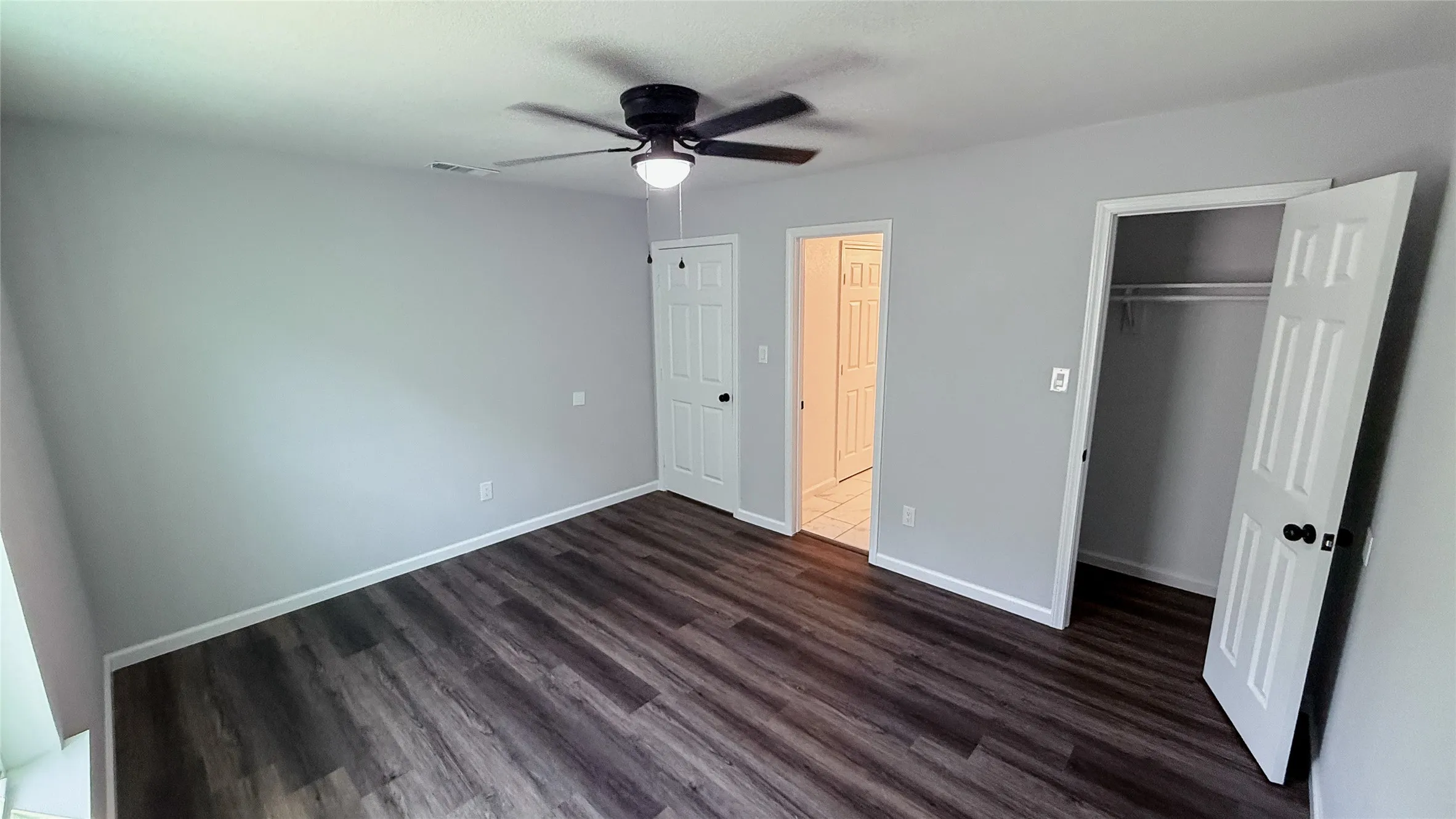 Room featuring wood-finish flooring, a ceiling fan with integrated lighting, and a closet with a built-in hanging rod