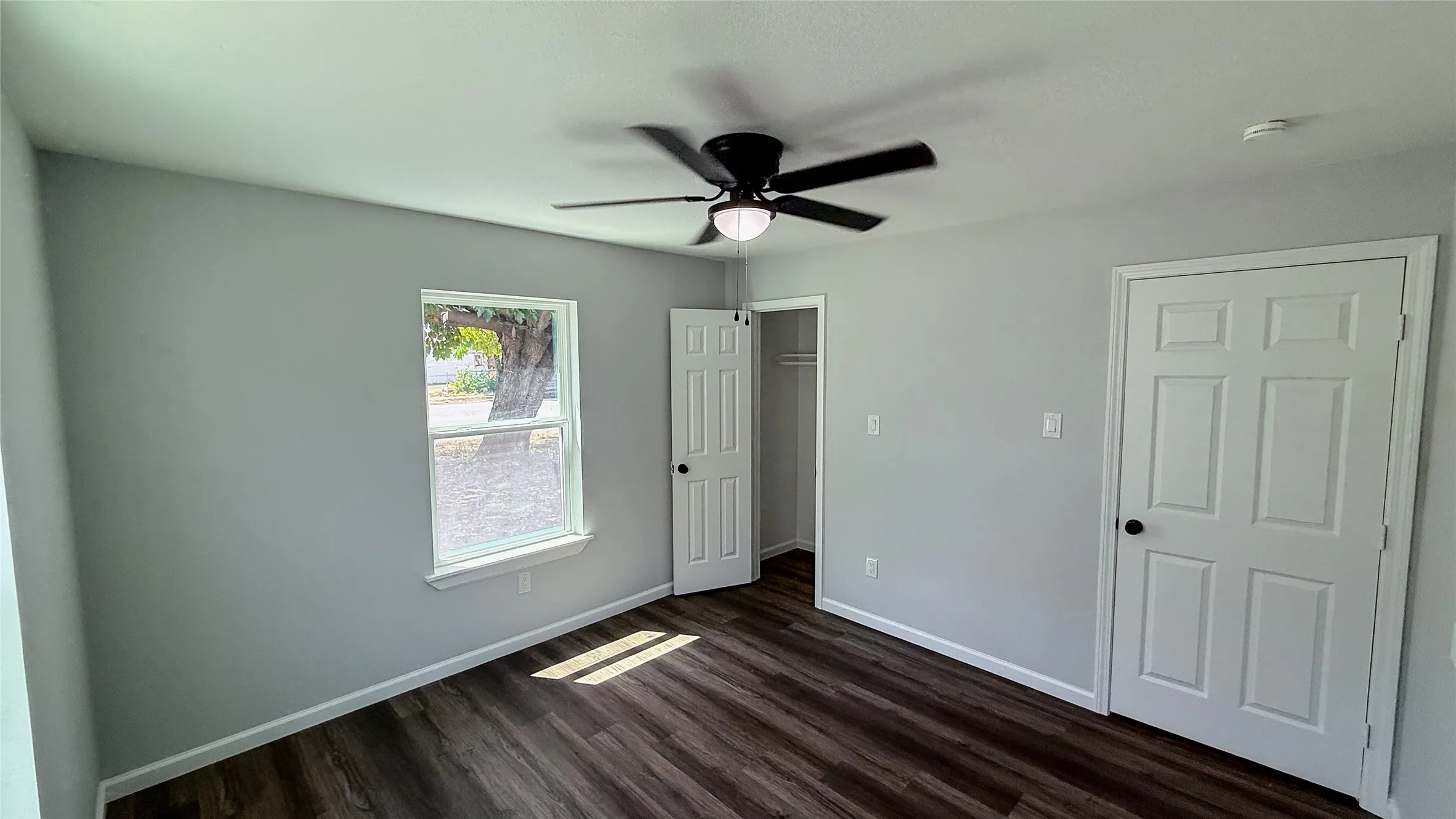 Light gray walls, wood-finish flooring, white trim, ceiling fan with integrated lighting, and white six-panel door