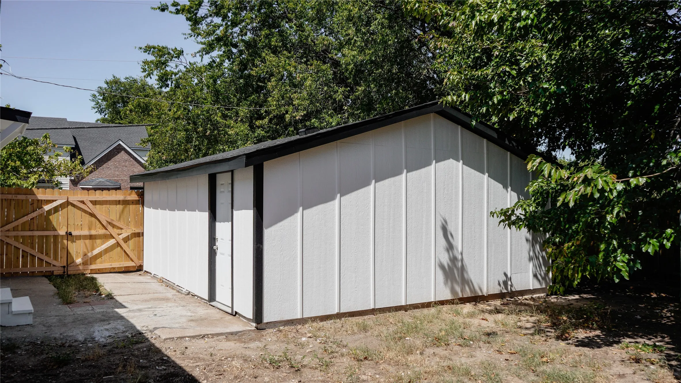 Detached storage shed with white siding and a black trim roofline