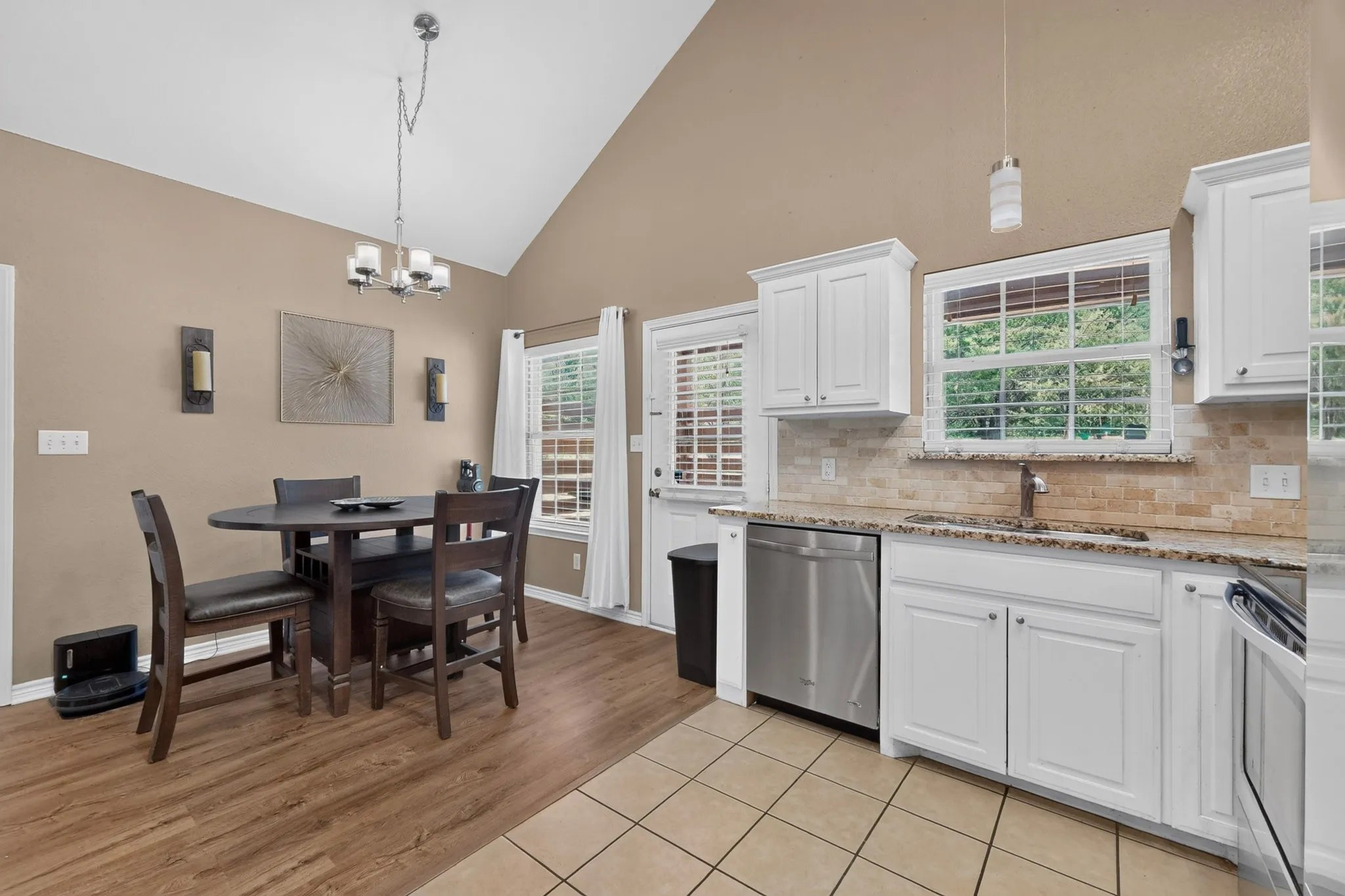 Vaulted ceiling, wood-finish flooring, white cabinetry, stainless steel dishwasher, and tiled backsplash