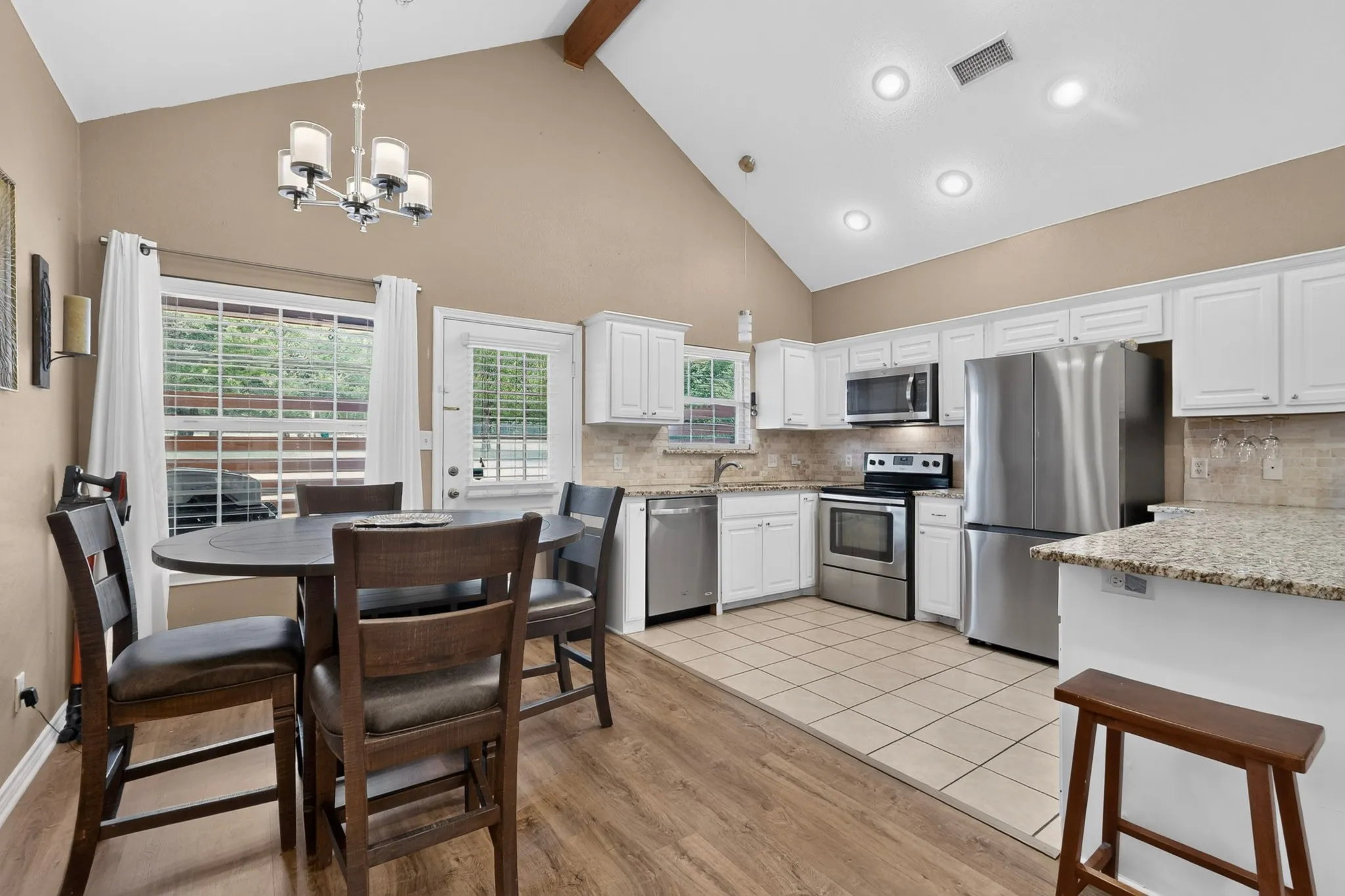 Vaulted ceiling with exposed wood beam, white cabinetry, stainless steel appliances, tile flooring, and wood-finish flooring
