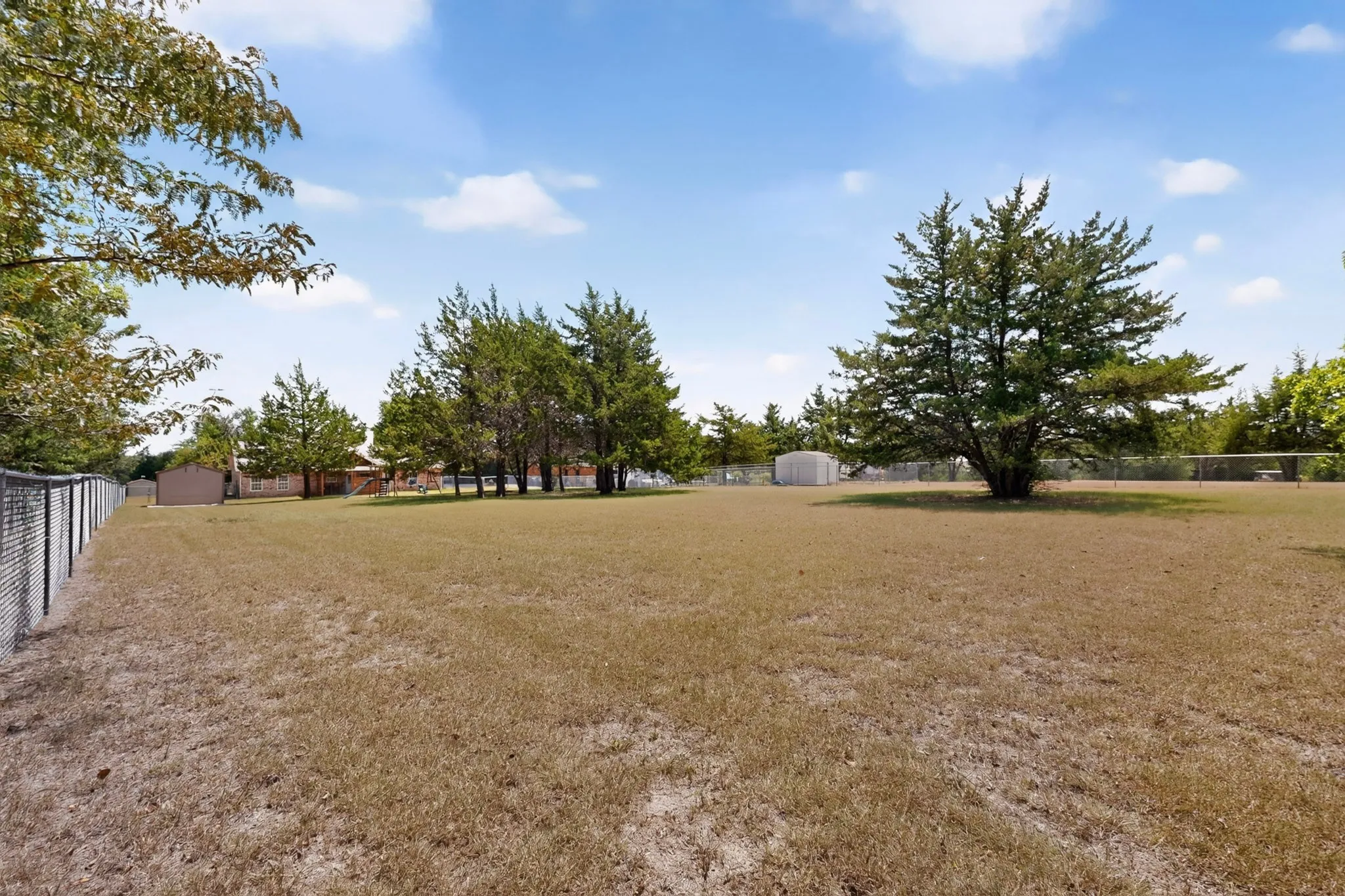 Expansive fenced yard with mature trees and a storage shed