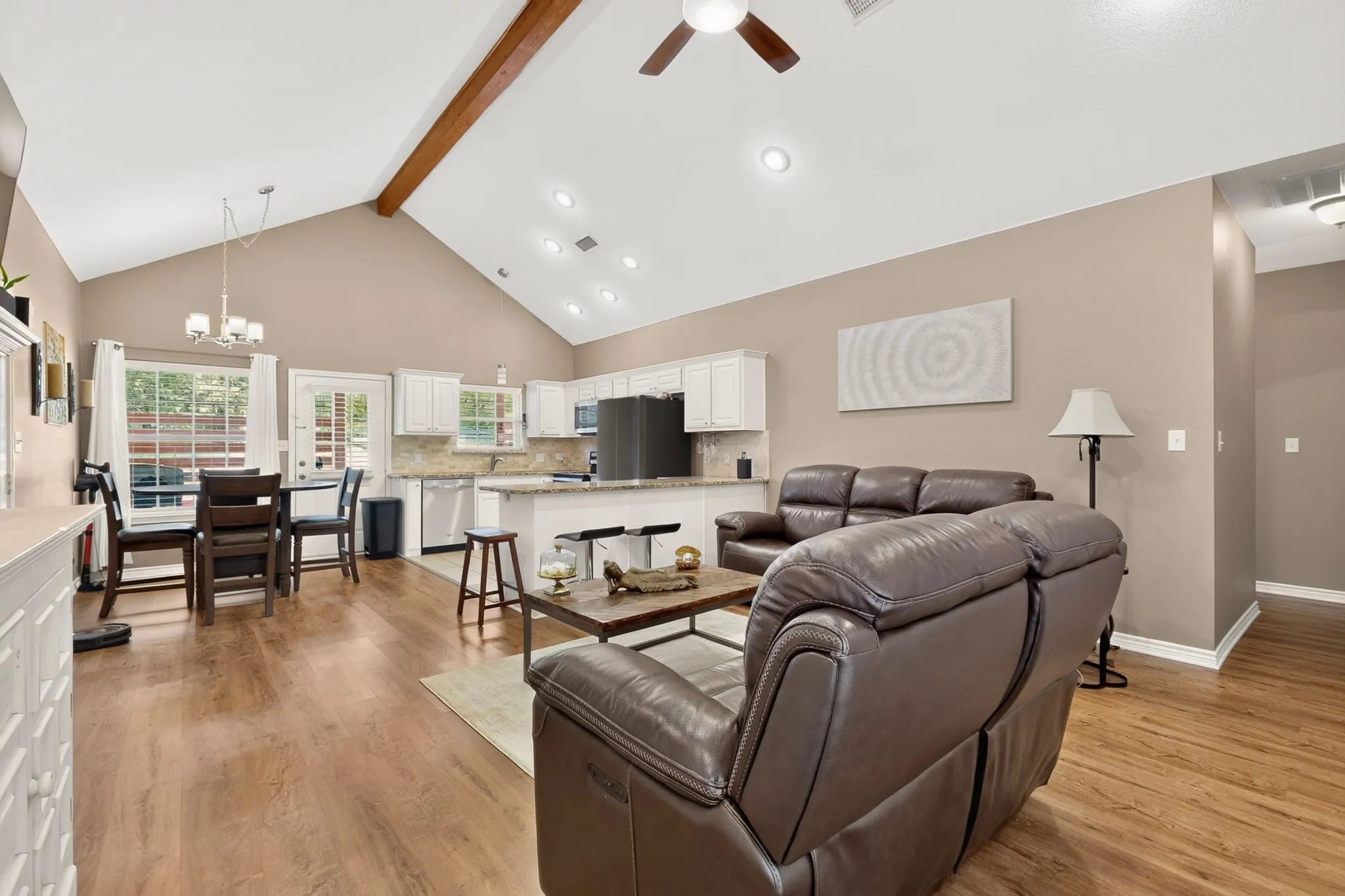 Vaulted ceilings with exposed wood beam, recessed lighting, wood-finish flooring, white cabinetry, and a kitchen island with seating