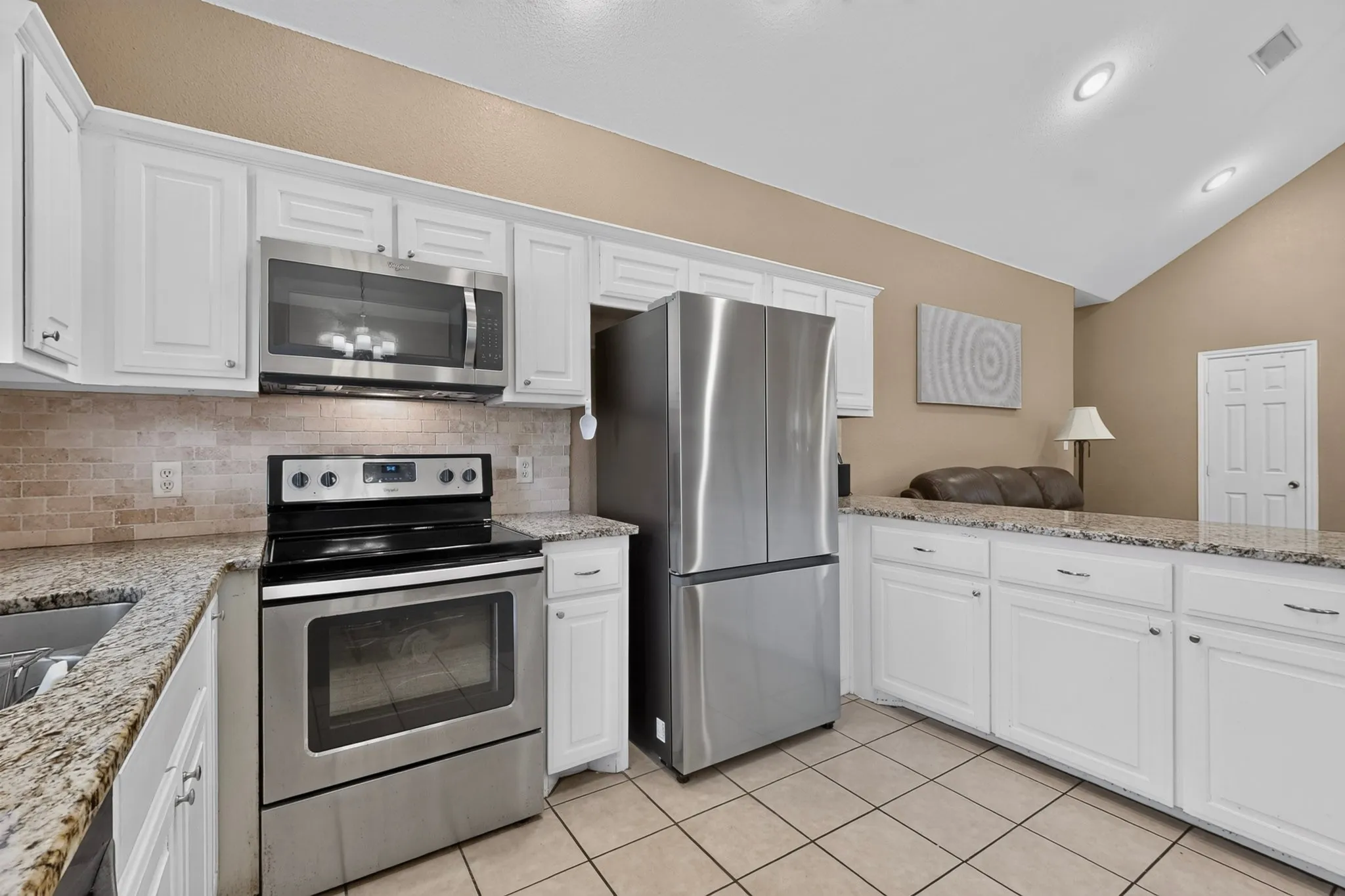 White cabinetry with stainless steel appliances, speckled stone countertops, and a tiled backsplash