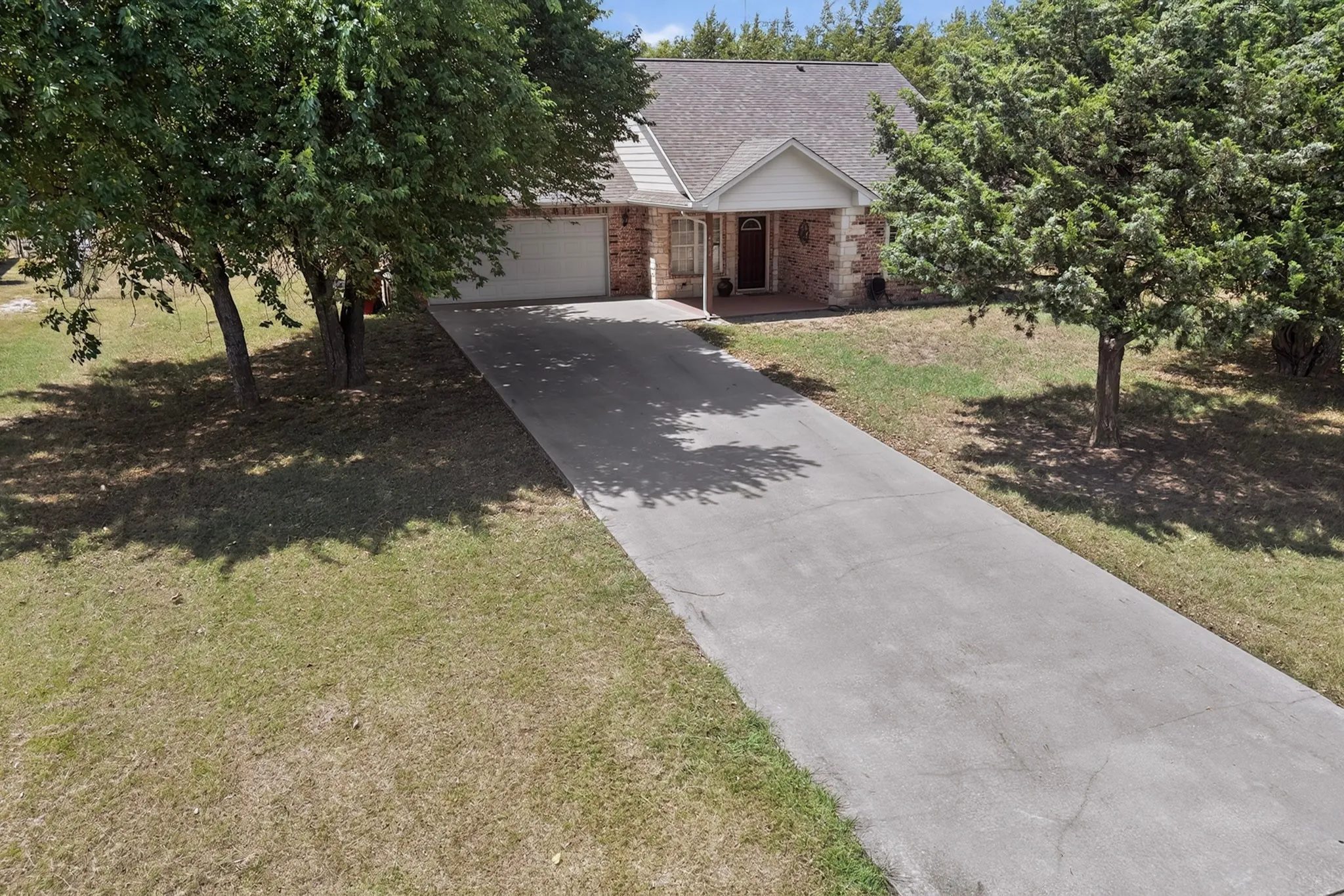 Brick exterior with a covered porch, attached garage, and paved driveway