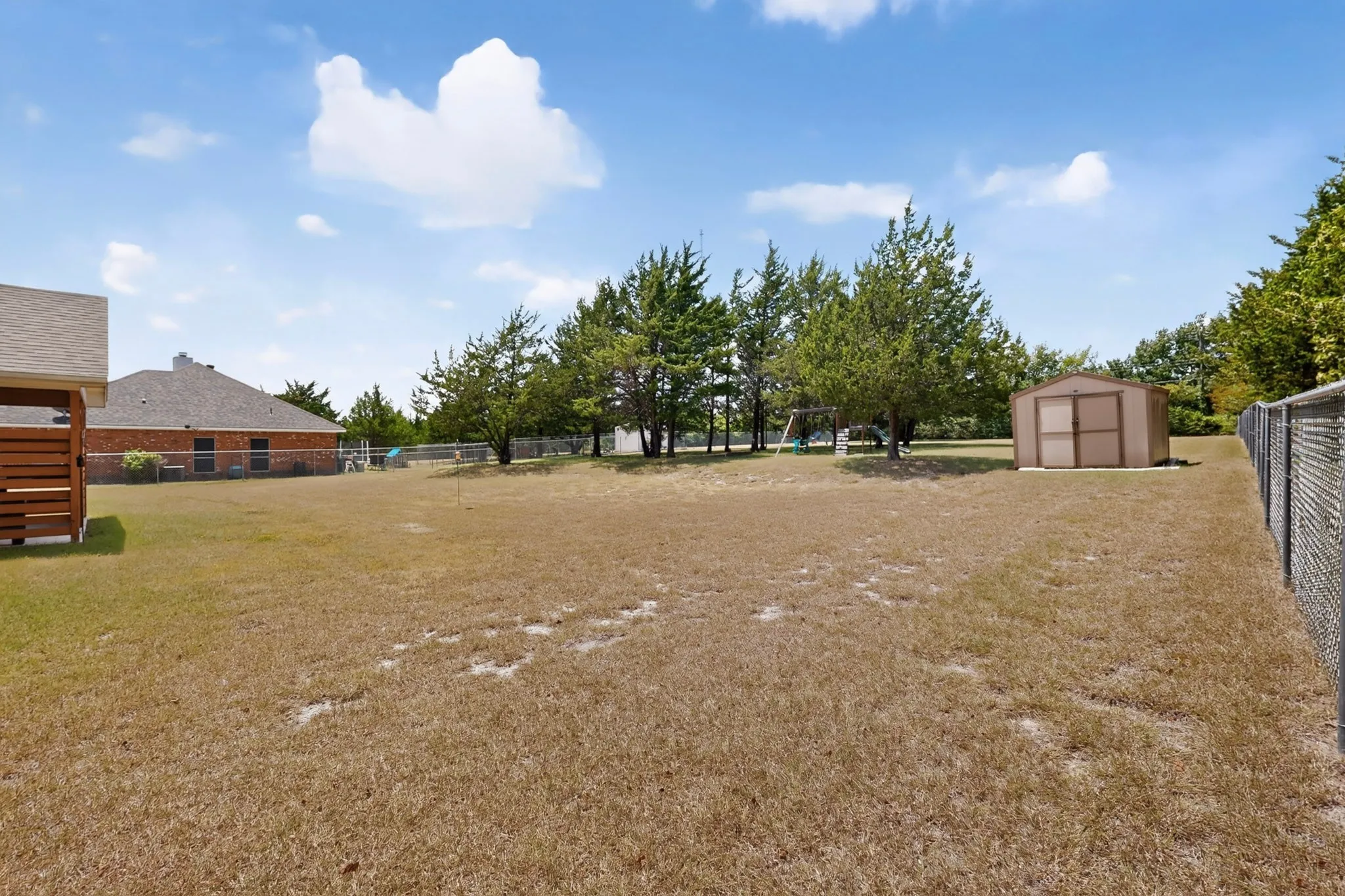 Expansive yard space featuring a chain-link perimeter fence, mature trees, and a freestanding storage shed