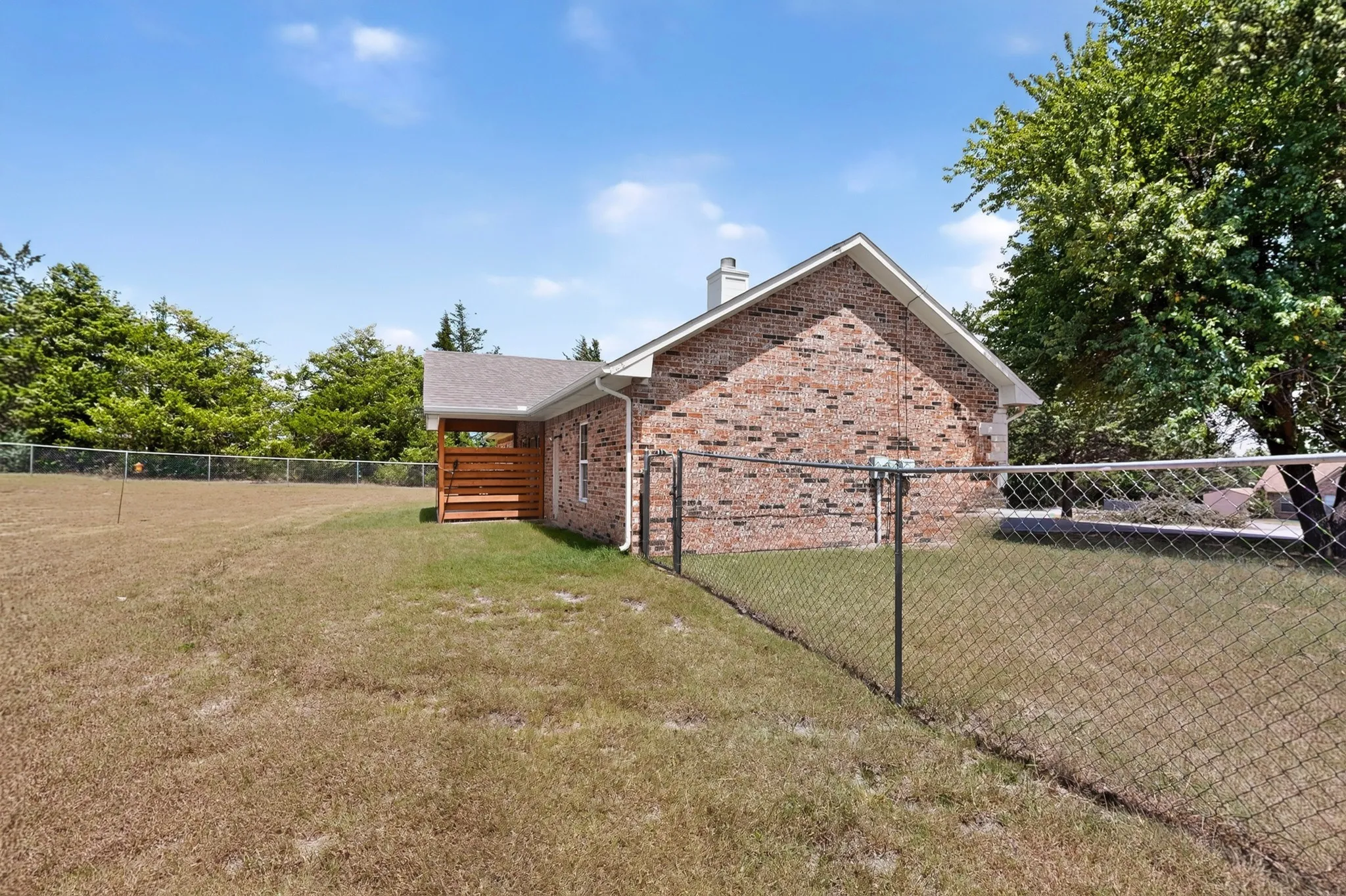 Brick exterior with a covered patio, chain link fencing, and a chimney