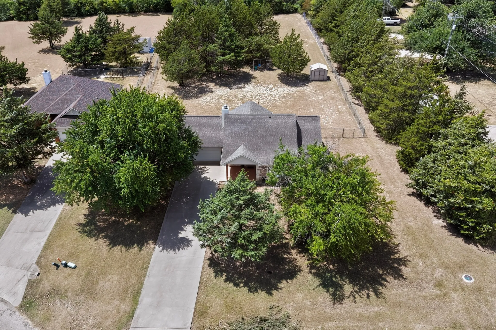 Expansive property featuring a paved driveway, mature trees, and a detached storage shed