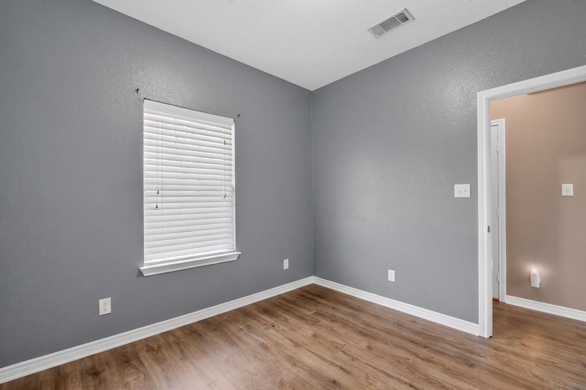Wood-finish flooring, white window blinds, and neutral painted walls