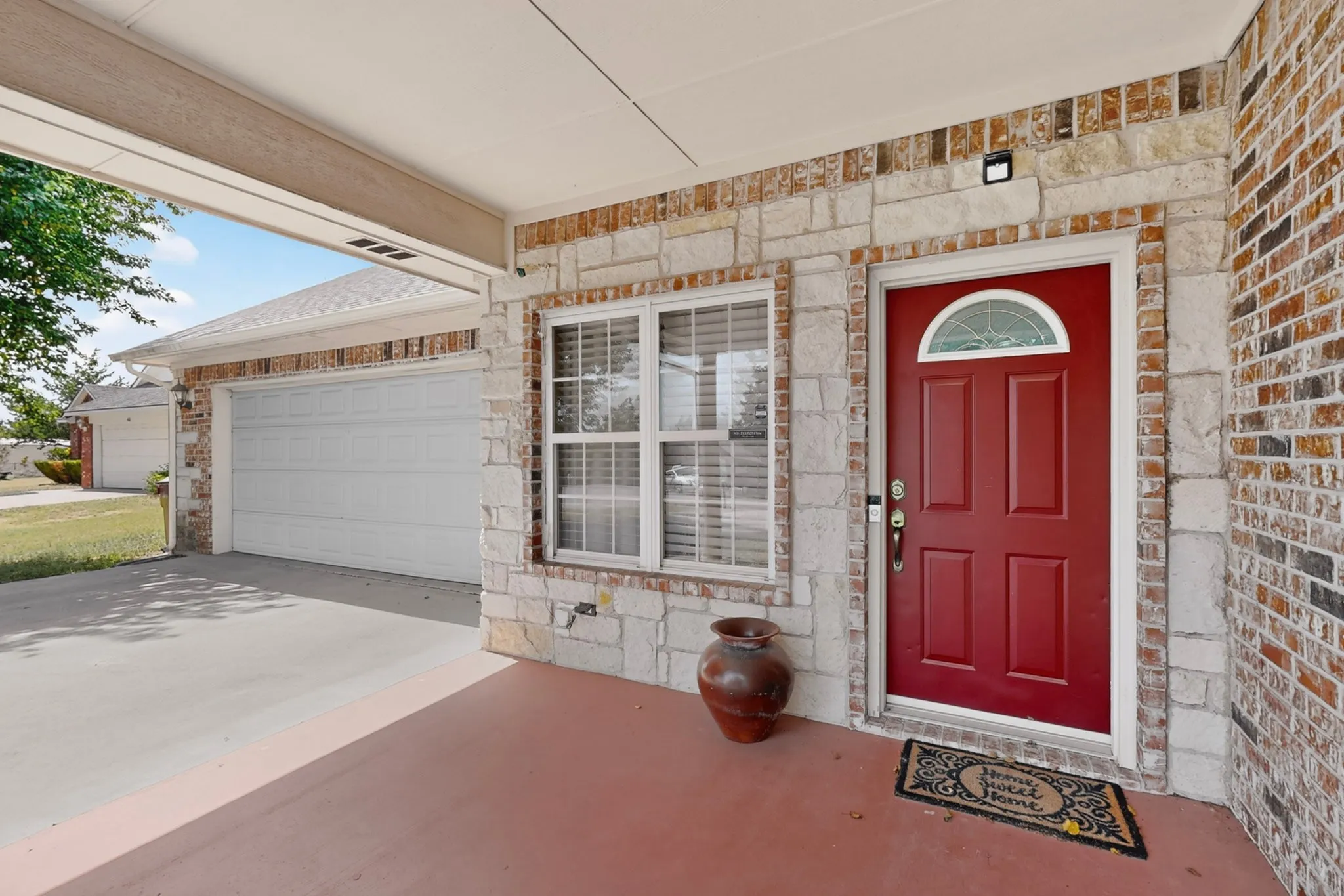 Stone and brick veneer exterior featuring a red entry door with an arched transom, a double-pane window, and an attached garage with a white door