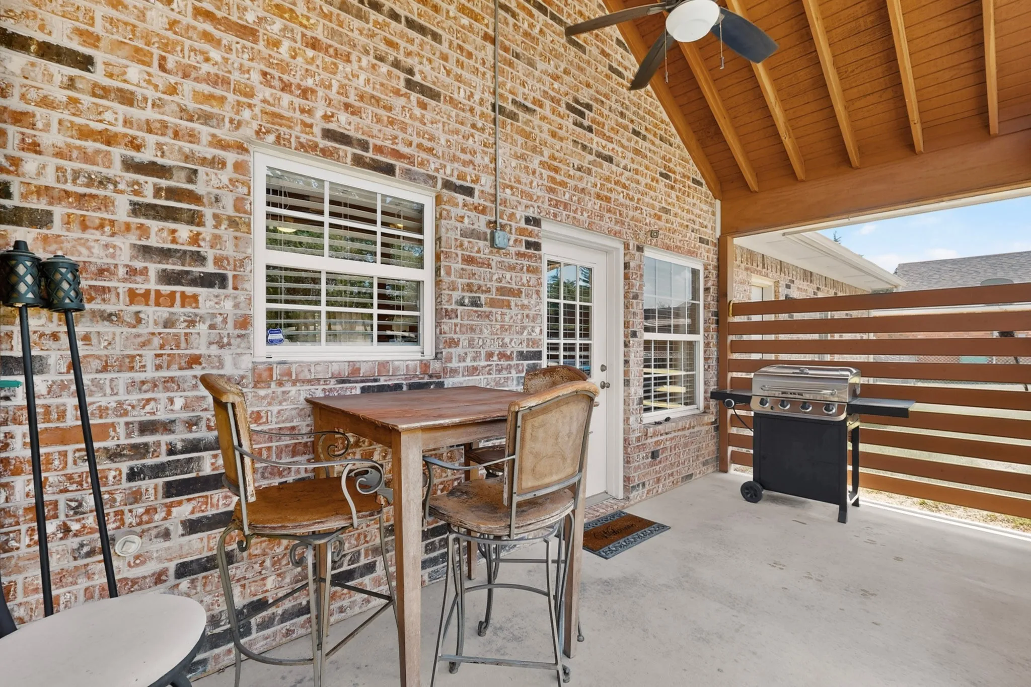 Covered patio featuring a ceiling fan, brick exterior, and slatted privacy screen