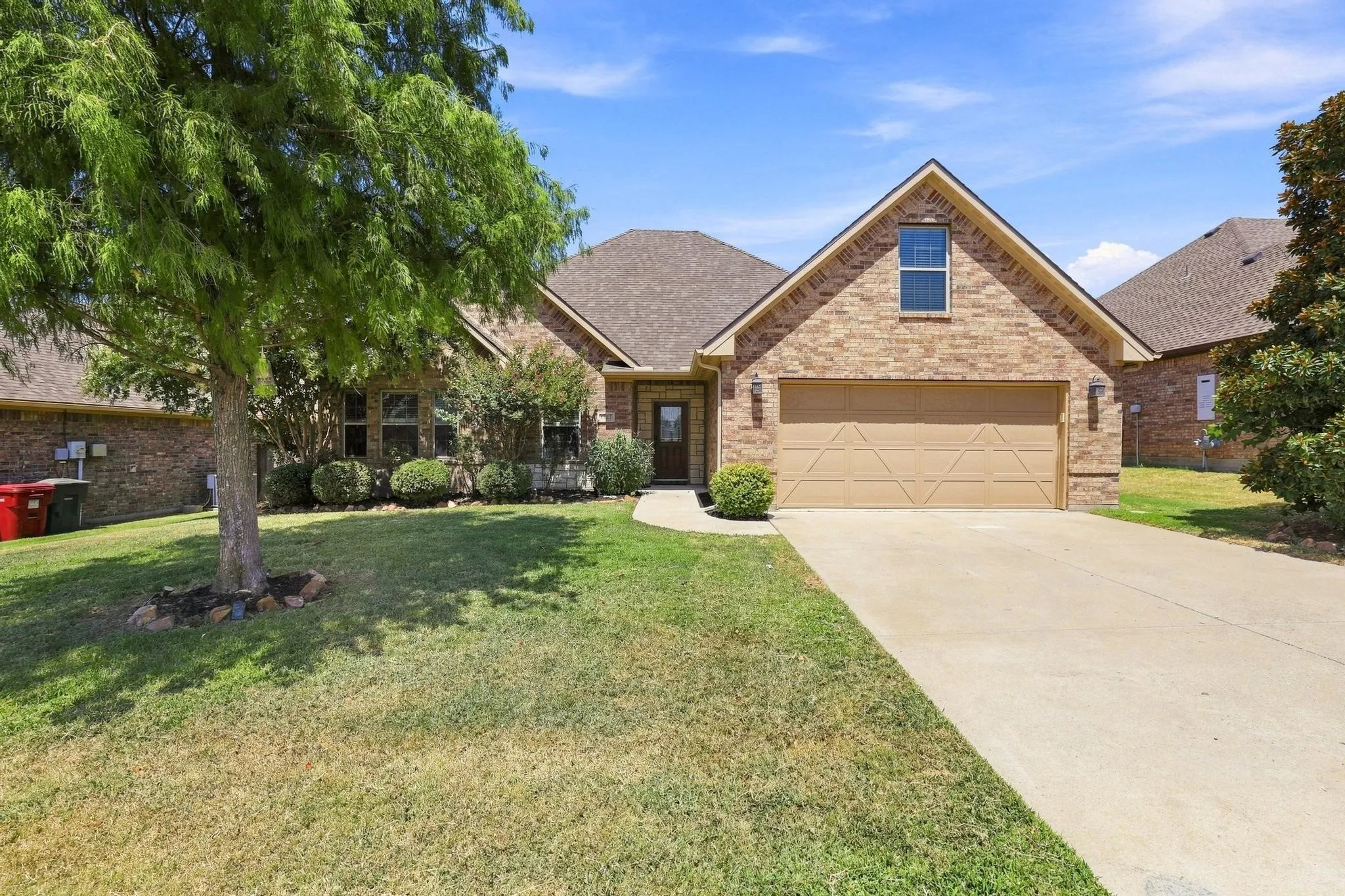 Brick exterior with an attached garage, pitched roof, and mature landscaping