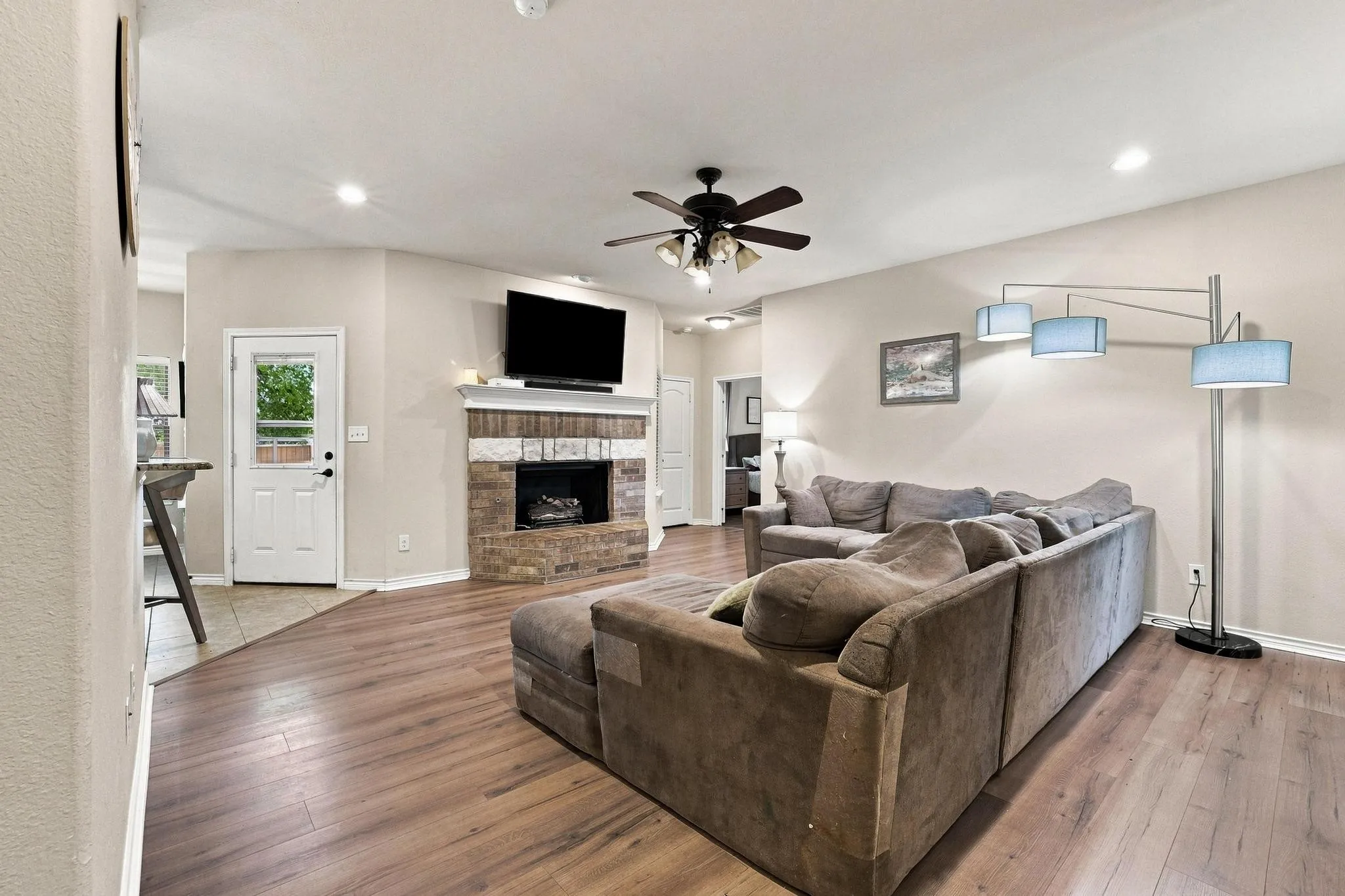 Spacious living area featuring wood-finish flooring, a ceiling fan, and a stone-clad fireplace with a white mantel