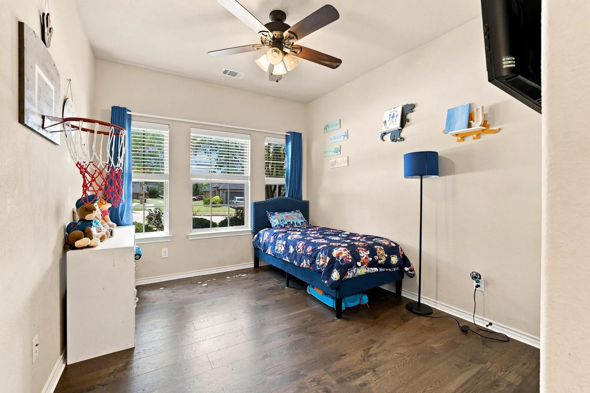 Hardwood-finish flooring, three windows with blinds, ceiling fan with light fixture, and neutral wall paint