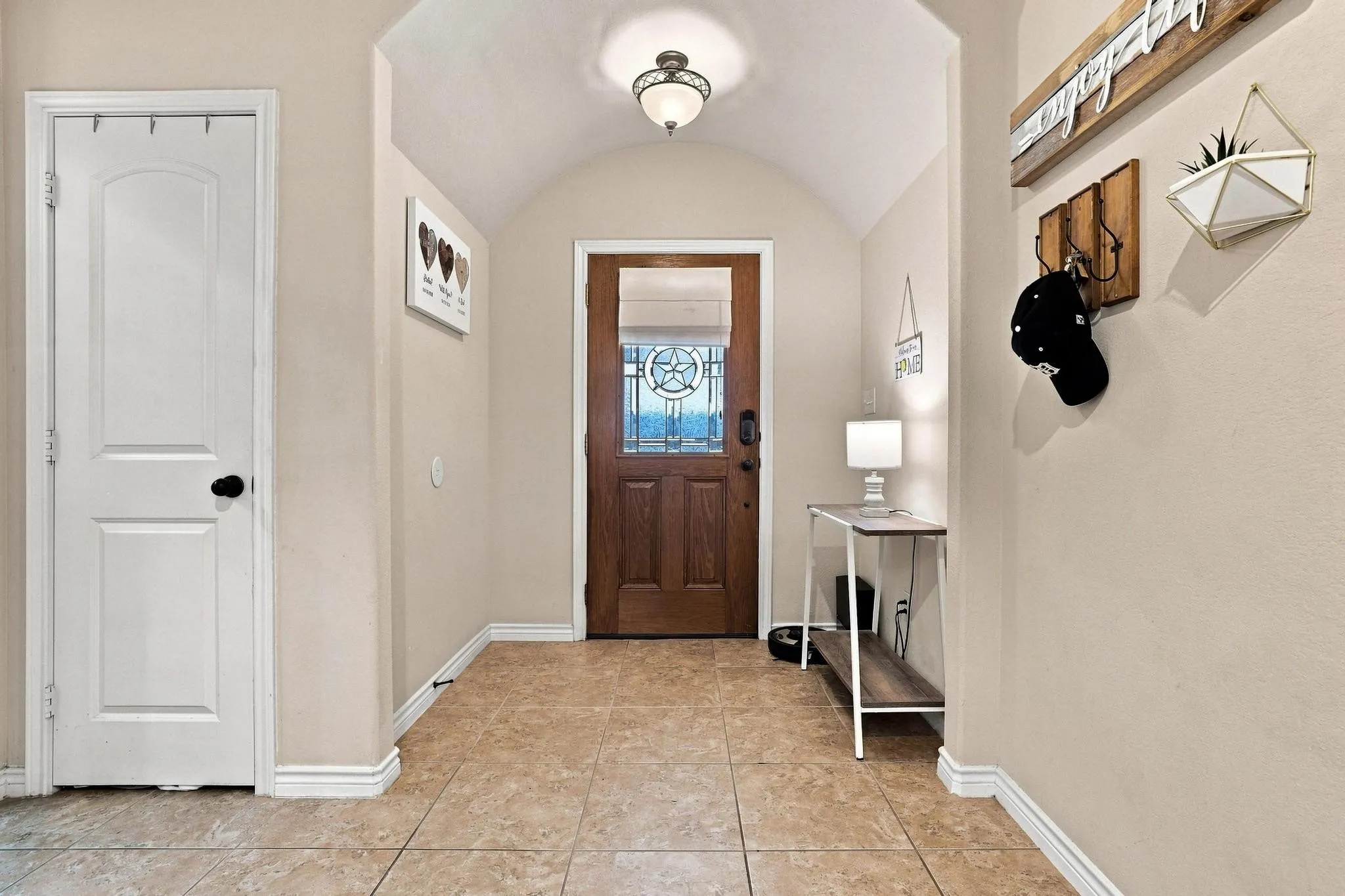 Arched entryway featuring a wood-finish door with decorative glass, recessed ceiling light, and light-toned tile flooring