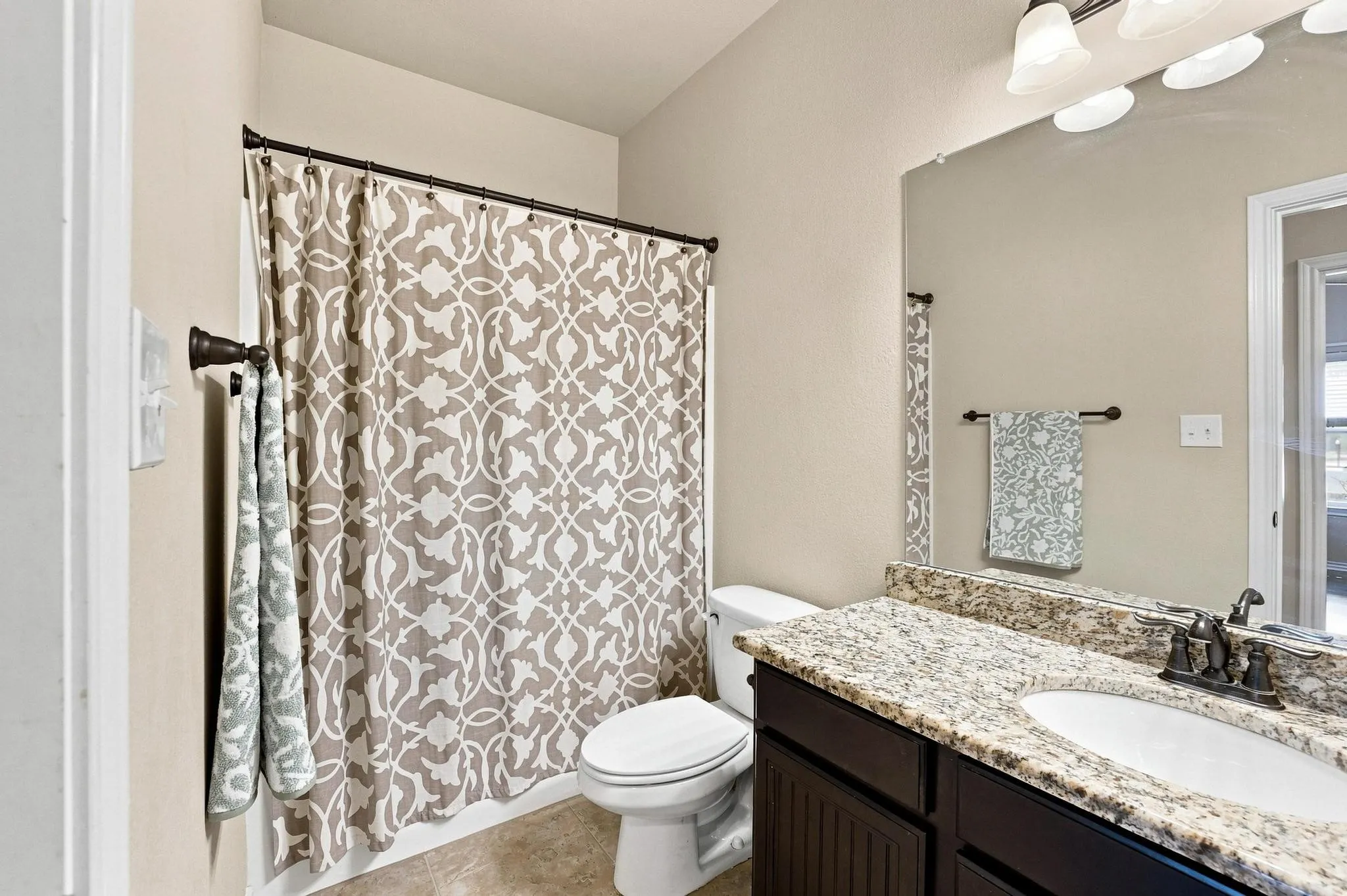 Bathroom featuring a shower with a patterned curtain, a dark wood-finish vanity with a single sink, a light-colored stone countertop, and a wall-mounted mirror