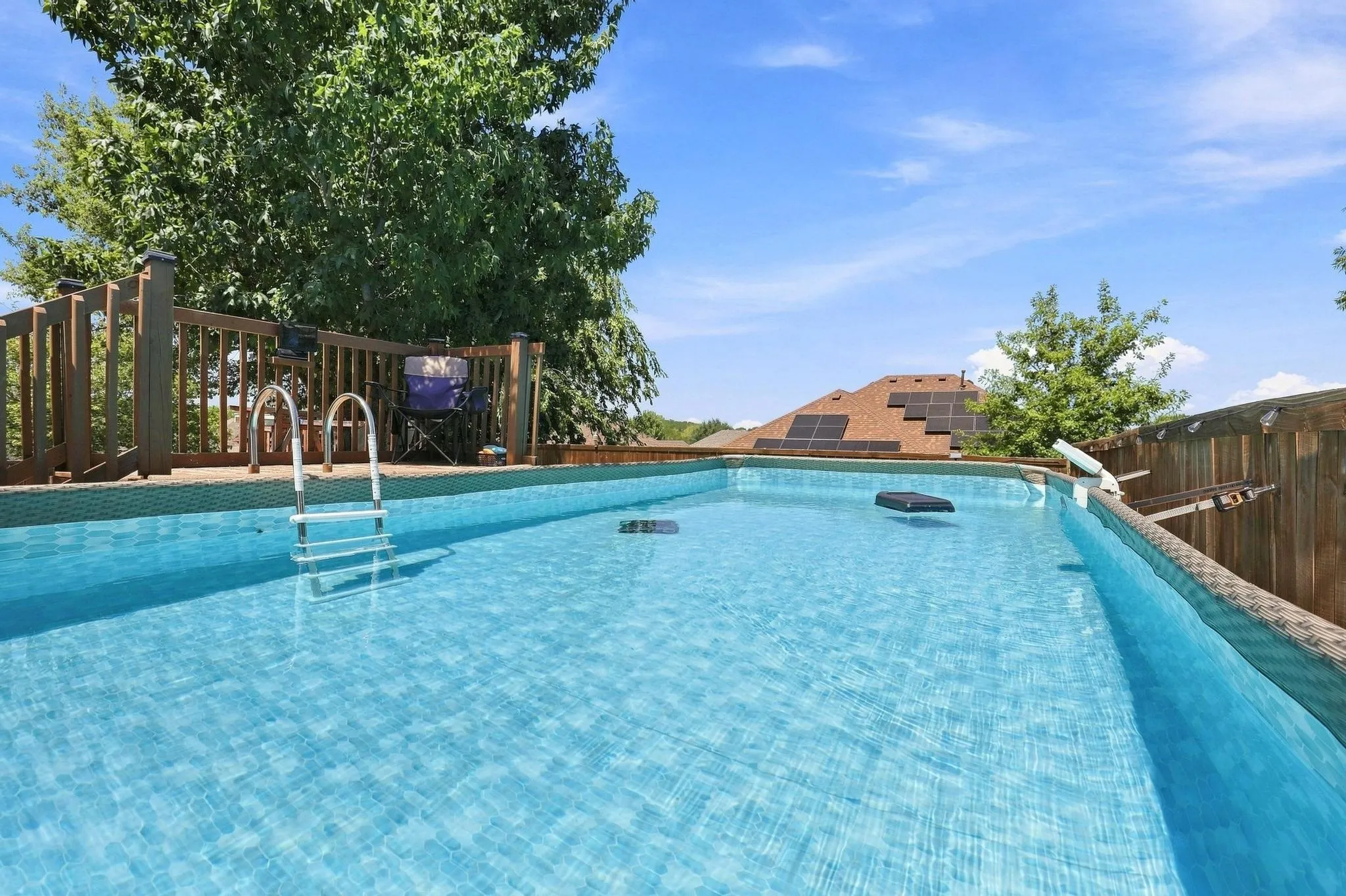 Swimming pool with a ladder, wood-finish deck with railing, and a privacy fence